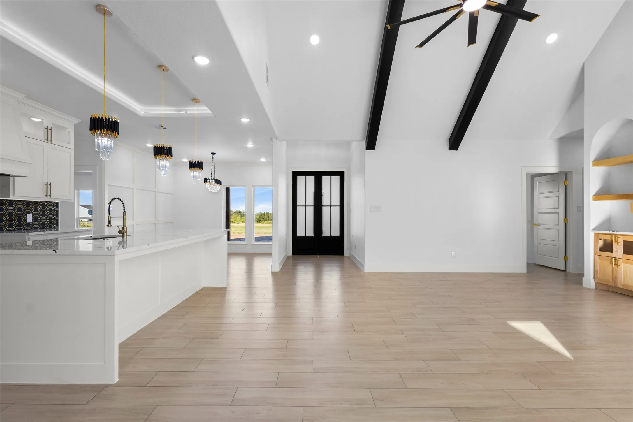 Vaulted ceiling with exposed beams, wood-finish flooring, built-in shelving, white cabinetry, and a kitchen island with pendant lighting
