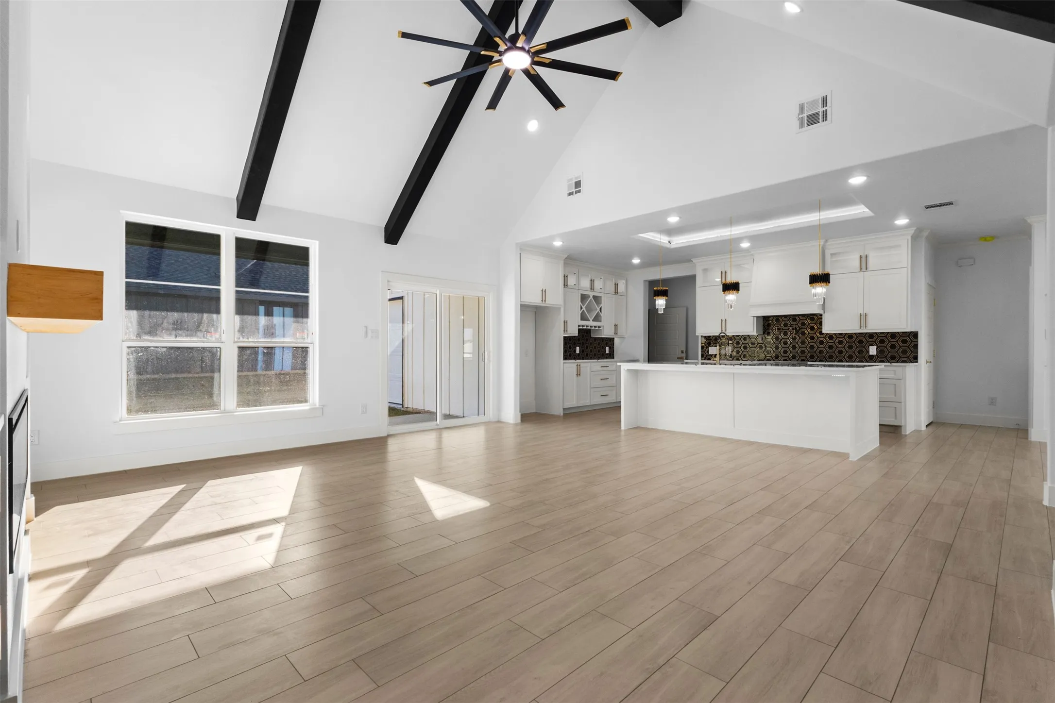 Vaulted ceiling with exposed beams, wood-finish flooring, white cabinetry, kitchen island with built-in sink, and patterned backsplash