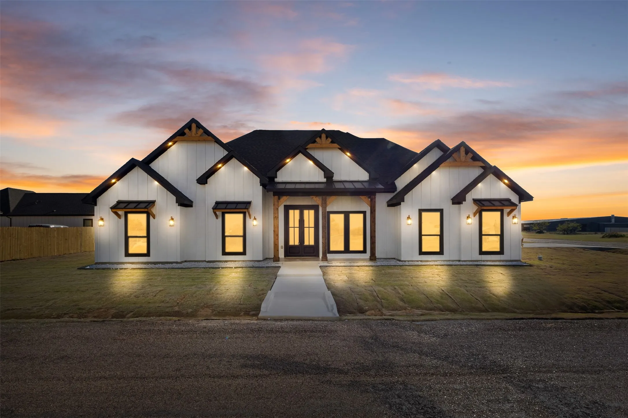 Modern farmhouse exterior with white vertical siding, black-framed windows, dark roofing, and exposed wood architectural accents