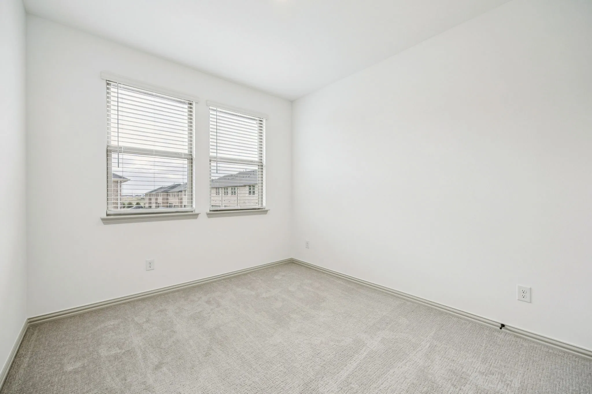 Neutral tone paint, light gray carpeting, and two windows with blinds