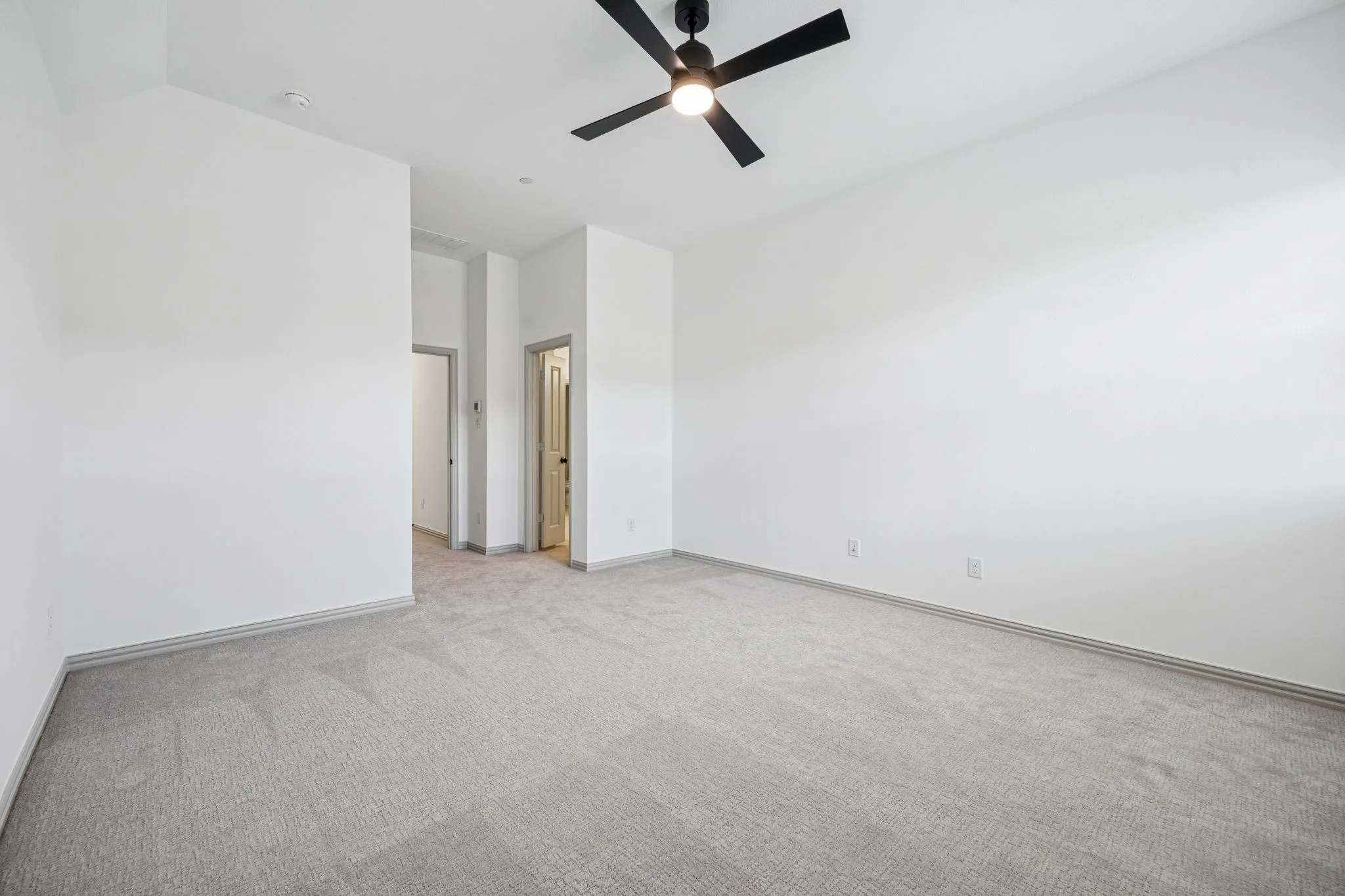 Expansive room featuring light gray carpeting, neutral wall paint, and a ceiling fan with integrated lighting