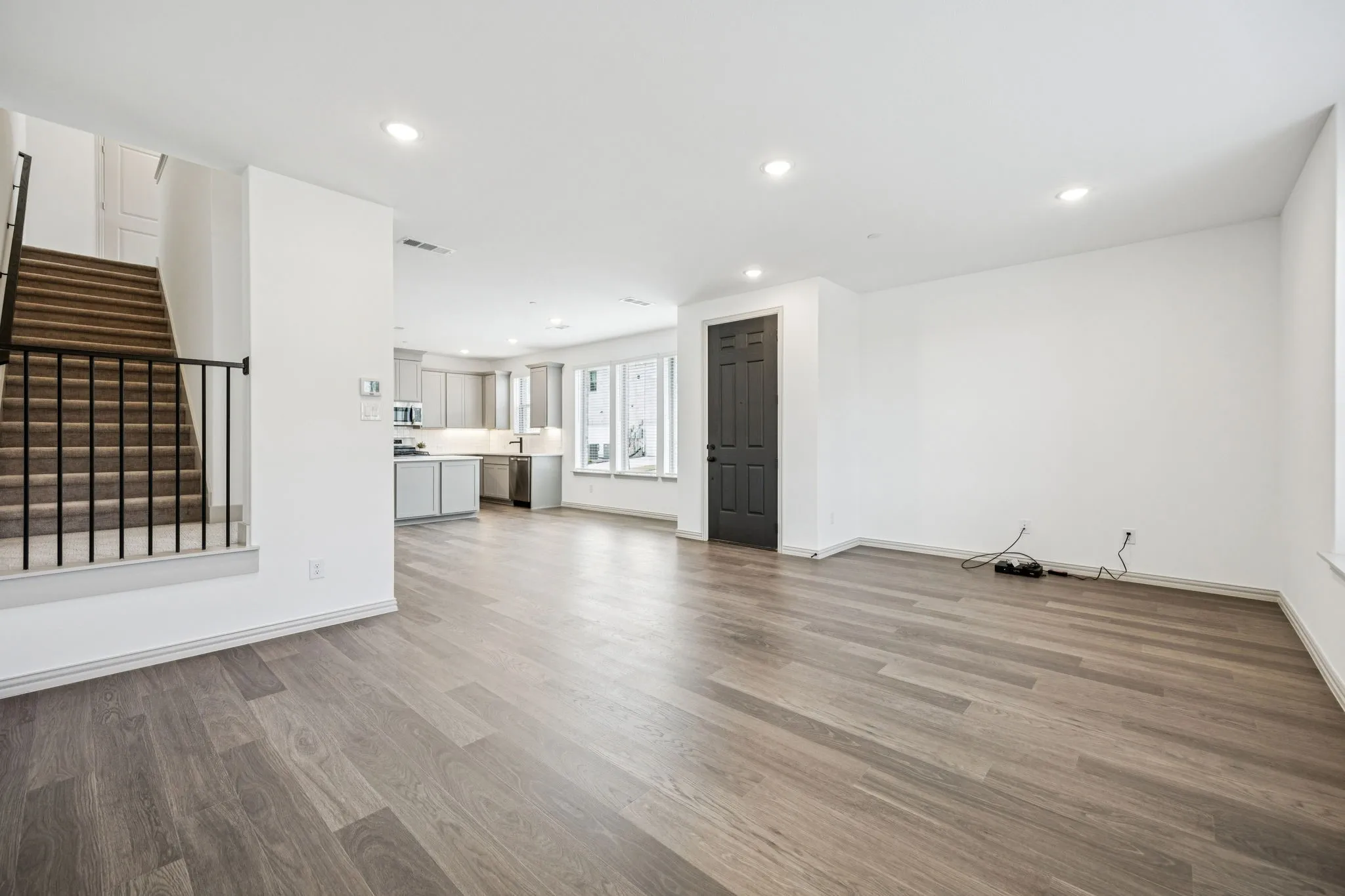 Open-concept living space featuring wood-finish flooring, recessed lighting, and a modern kitchen with grey cabinetry