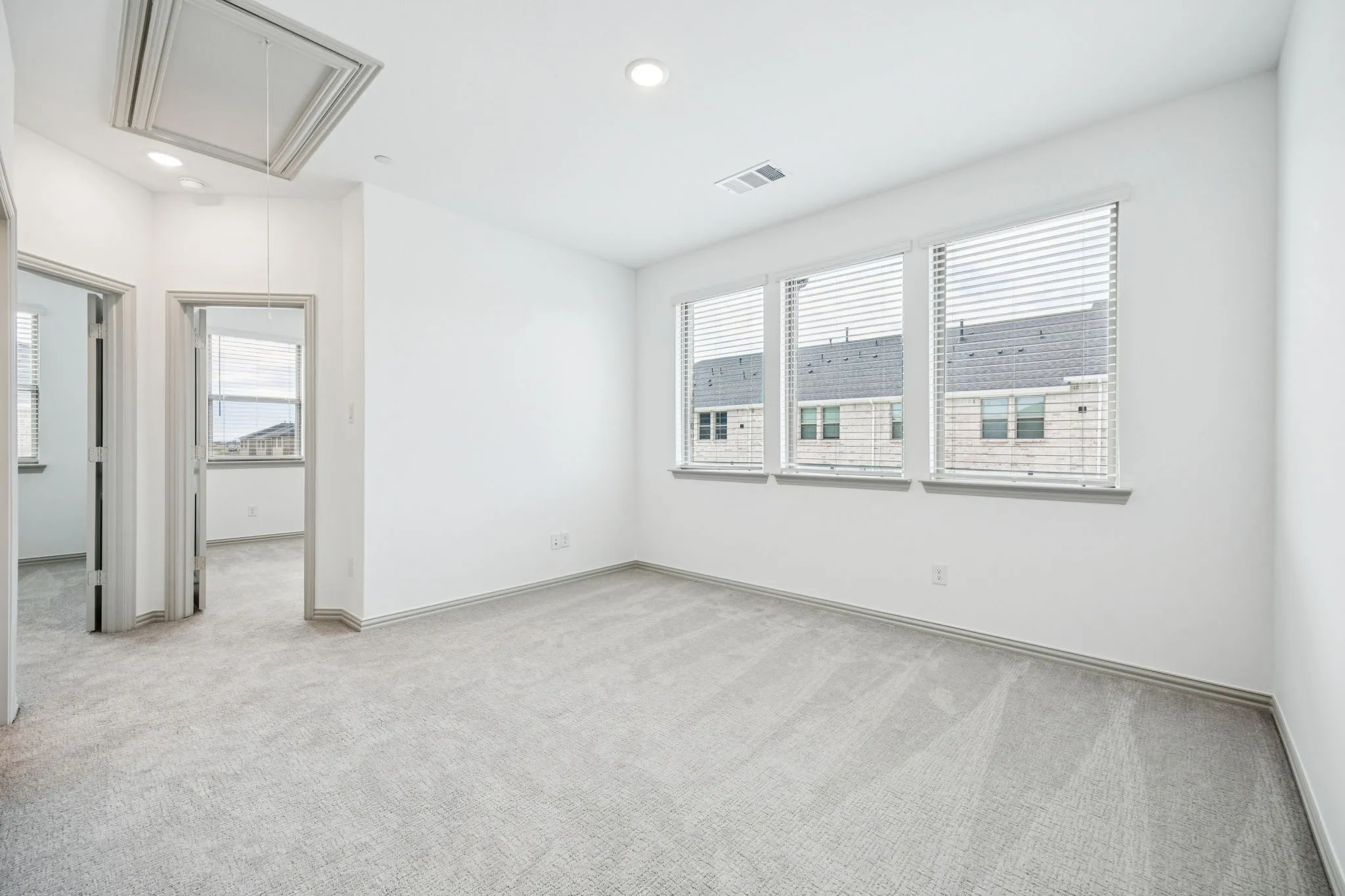 Plush carpet flooring, three windows with horizontal blinds, recessed lighting, and crisp white walls