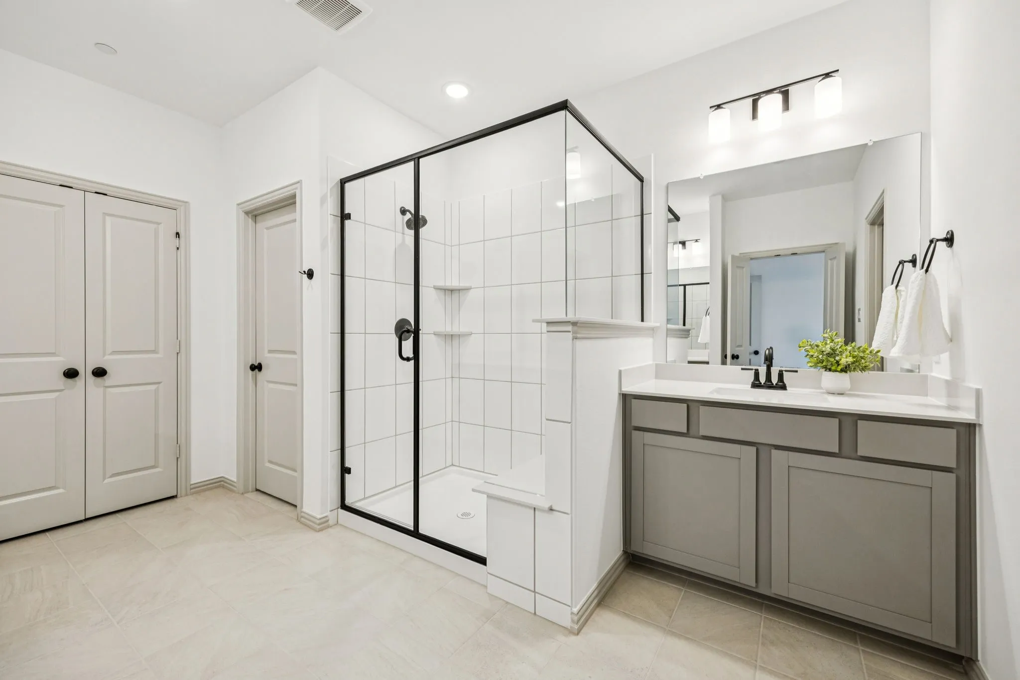 Bathroom featuring a glass-enclosed shower with black trim, a single vanity with gray cabinetry and white countertop, and tile flooring