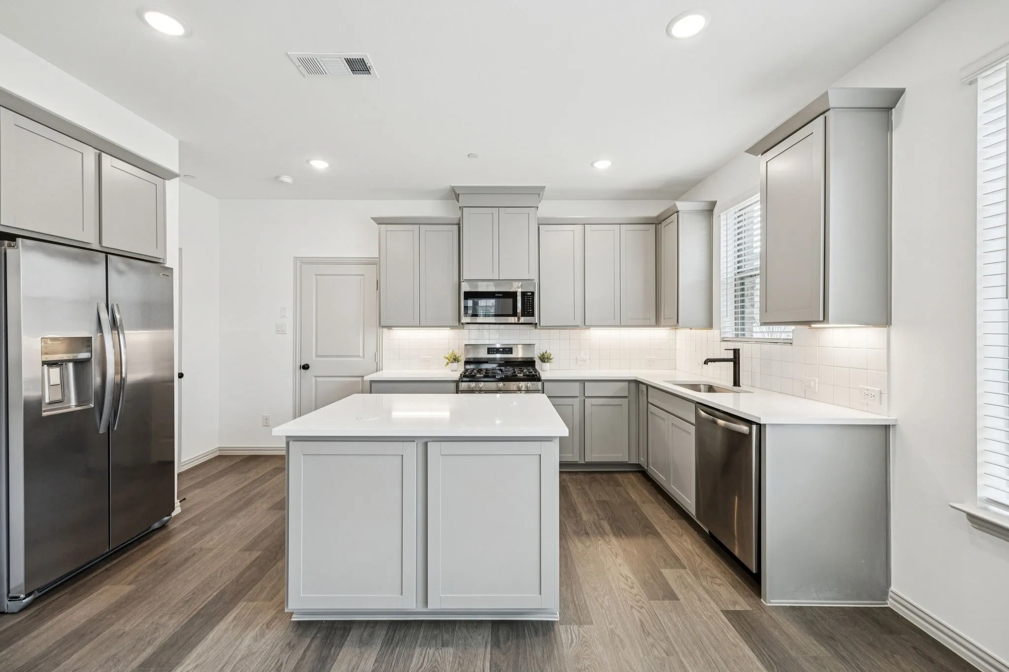 Modern kitchen featuring white countertops, stainless steel appliances, light gray cabinetry, wood-finish flooring, and recessed lighting