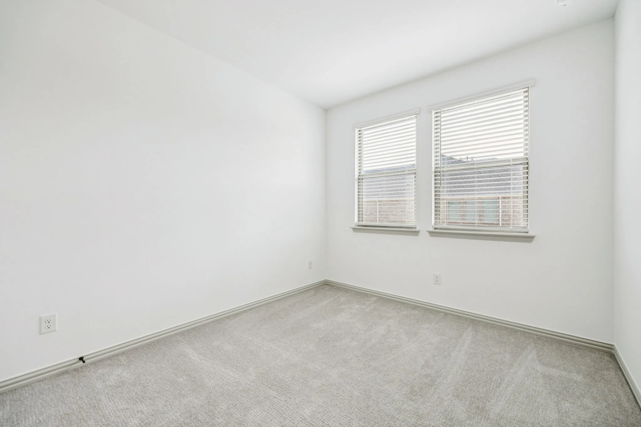 White painted walls, two rectangular windows with blinds, gray carpet, and recessed ceiling lighting