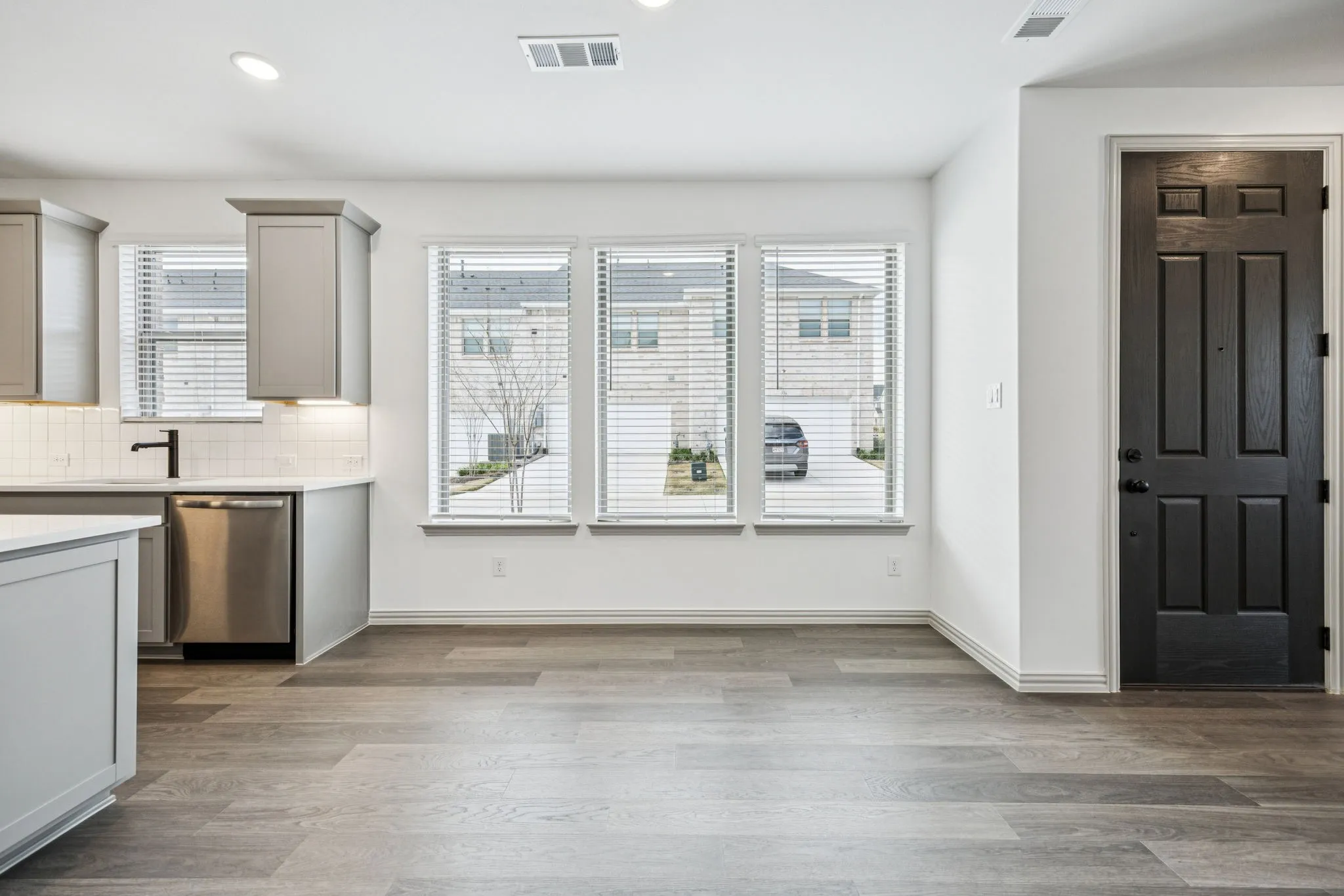 Kitchen area featuring gray cabinetry, white subway tile backsplash, stainless steel dishwasher, and wood-finish flooring