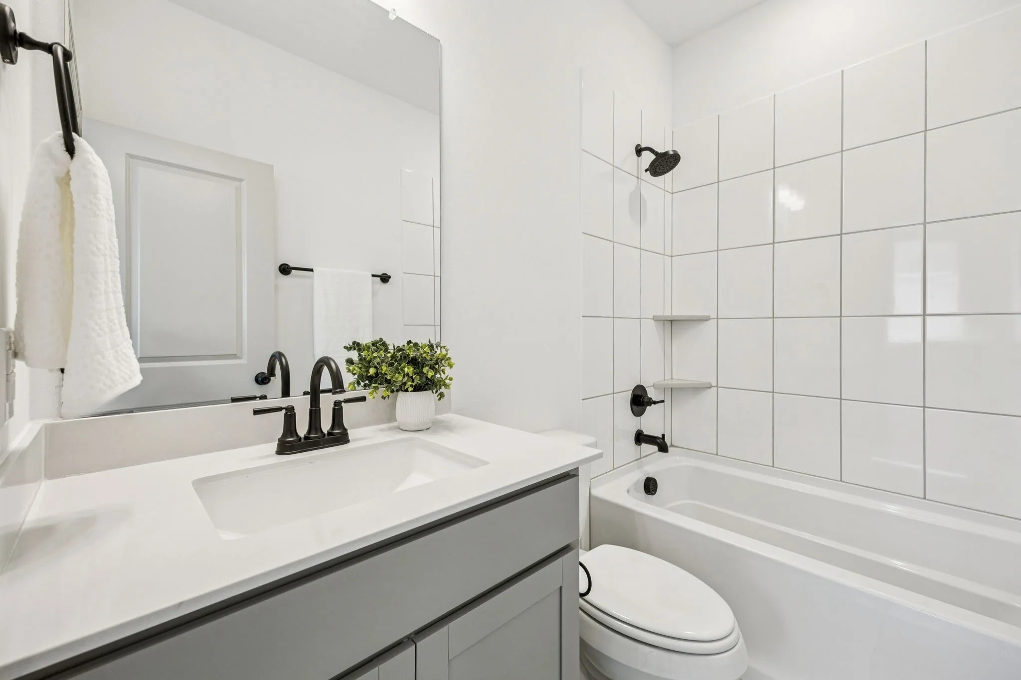 Integrated bathtub and shower with white tile surround, a single vanity with a white countertop and undermount sink, matte black fixtures, and a large wall-mounted mirror