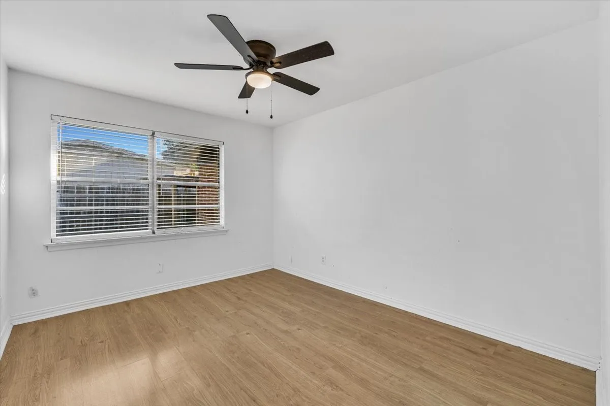 Wood-finish flooring, white walls, white trim, window with blinds, and a ceiling fan with light fixture