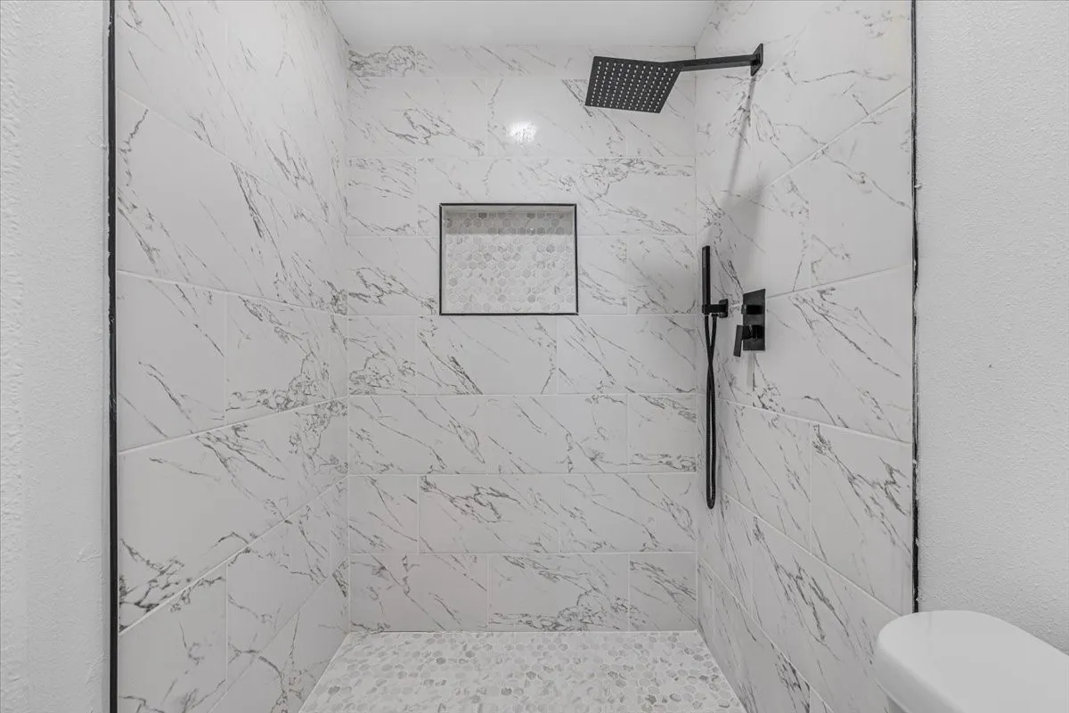 Walk-in shower featuring large format wall tile, a mosaic tile shower pan, a built-in shower niche, and matte black shower fixtures