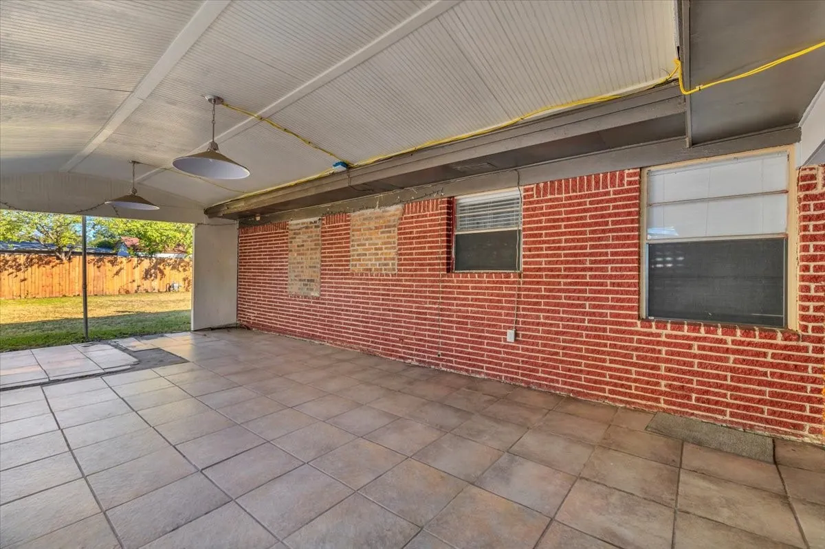 Covered patio featuring a tiled floor, brick wall, two pendant light fixtures, and a wood privacy fence