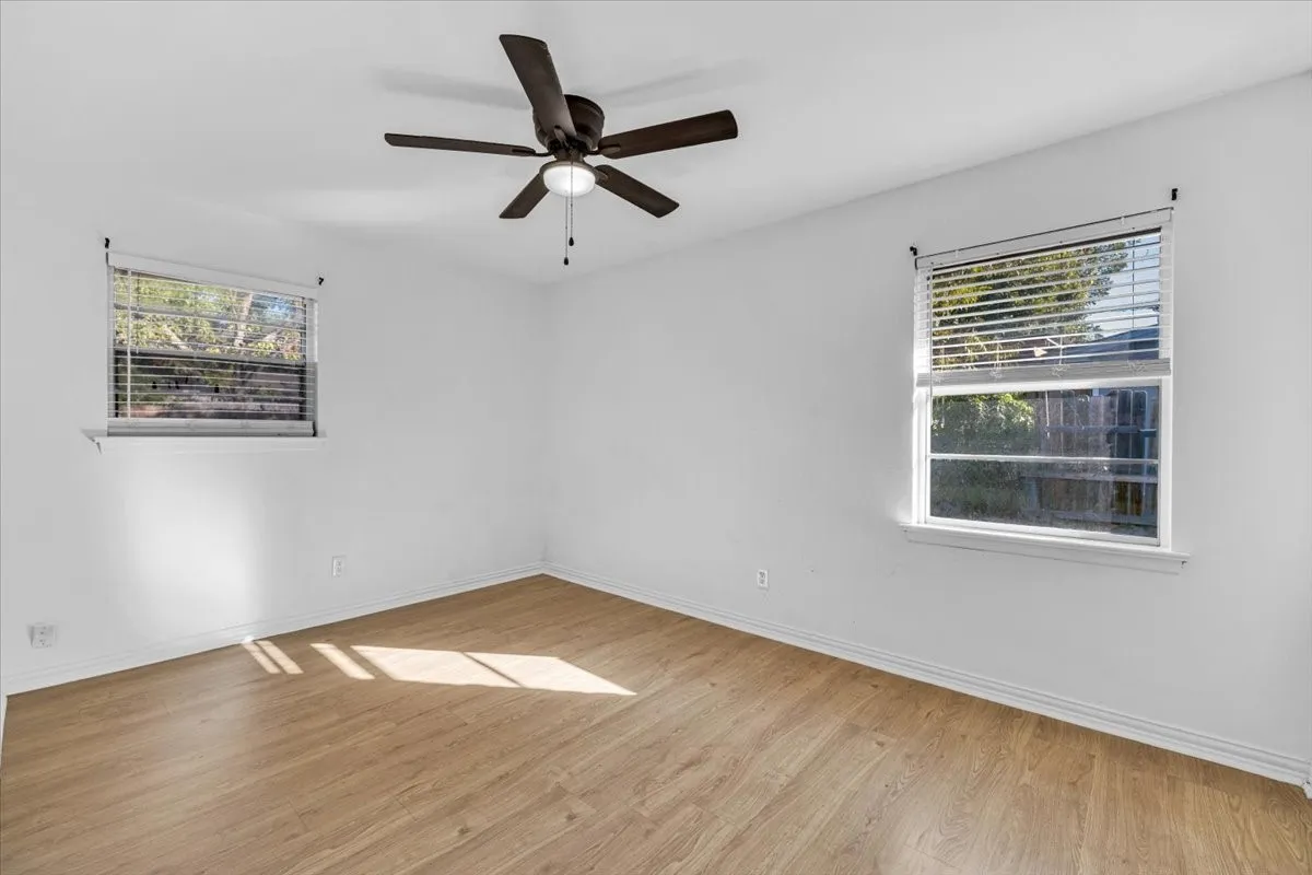 Wood-finish flooring, white walls, two windows, and a ceiling fan with integrated lighting