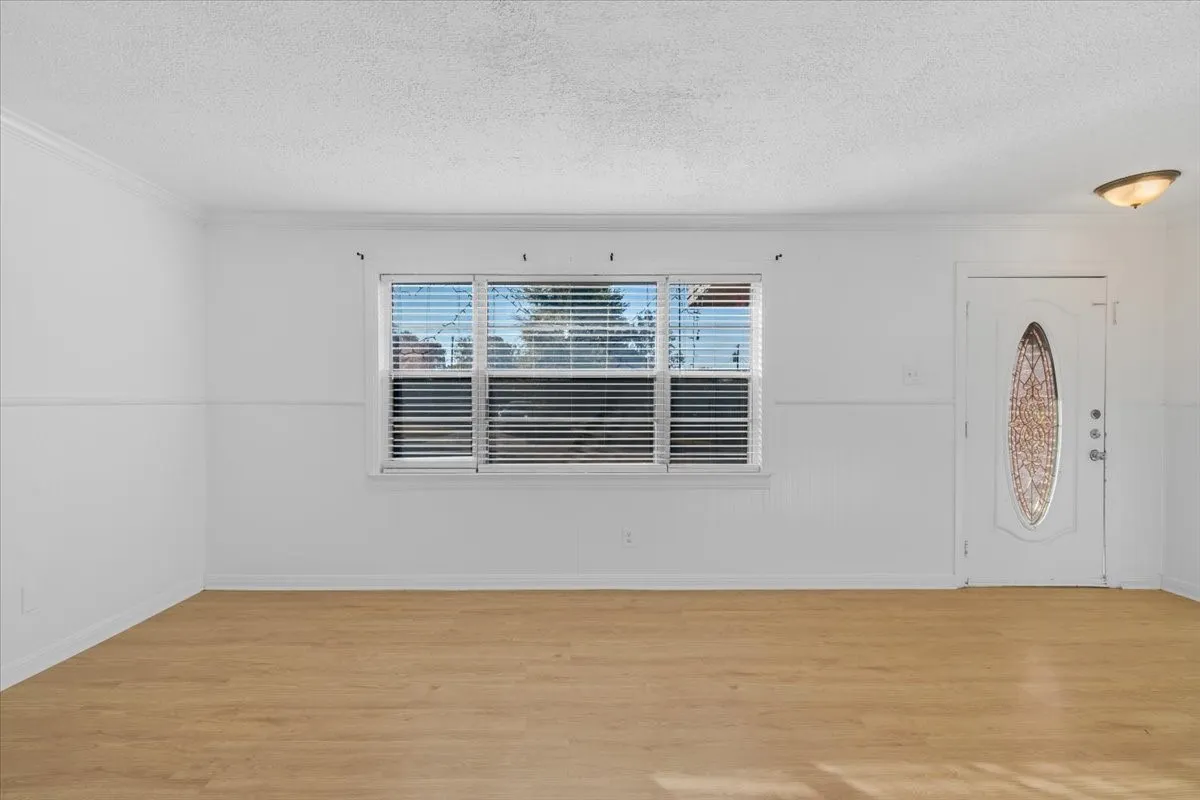 White interior walls, crown molding, wood-finish flooring, white entry door with decorative glass inlay, and a flush mount ceiling light