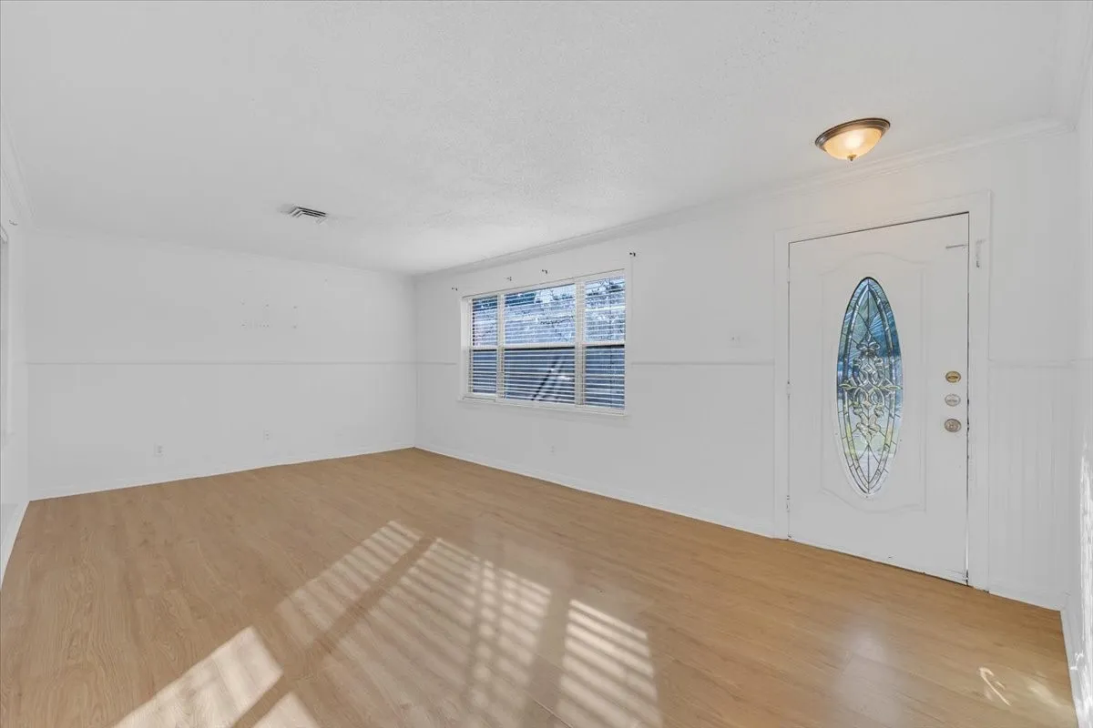 Wood-finish flooring, white walls, decorative front door with an oval stained-glass insert, and a flush mount ceiling light fixture