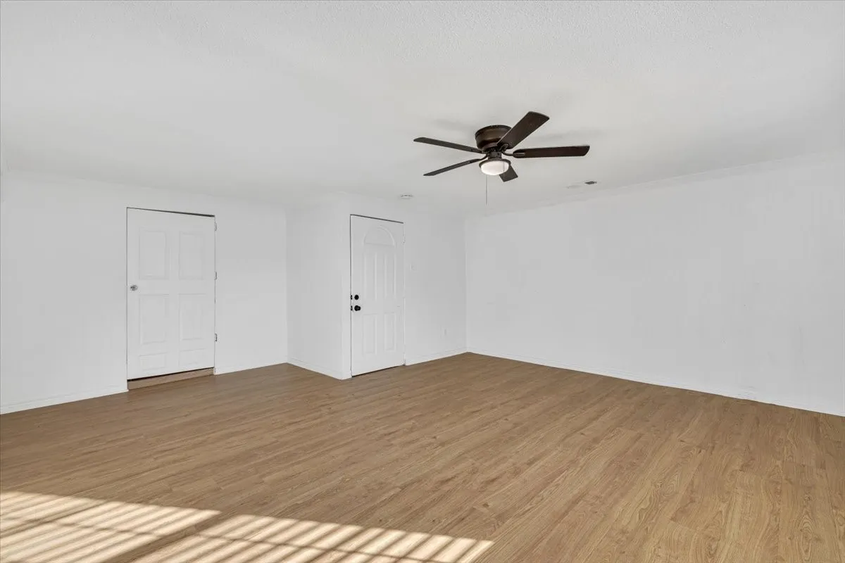 Wood-finish flooring, white walls, and a ceiling fan with integrated lighting