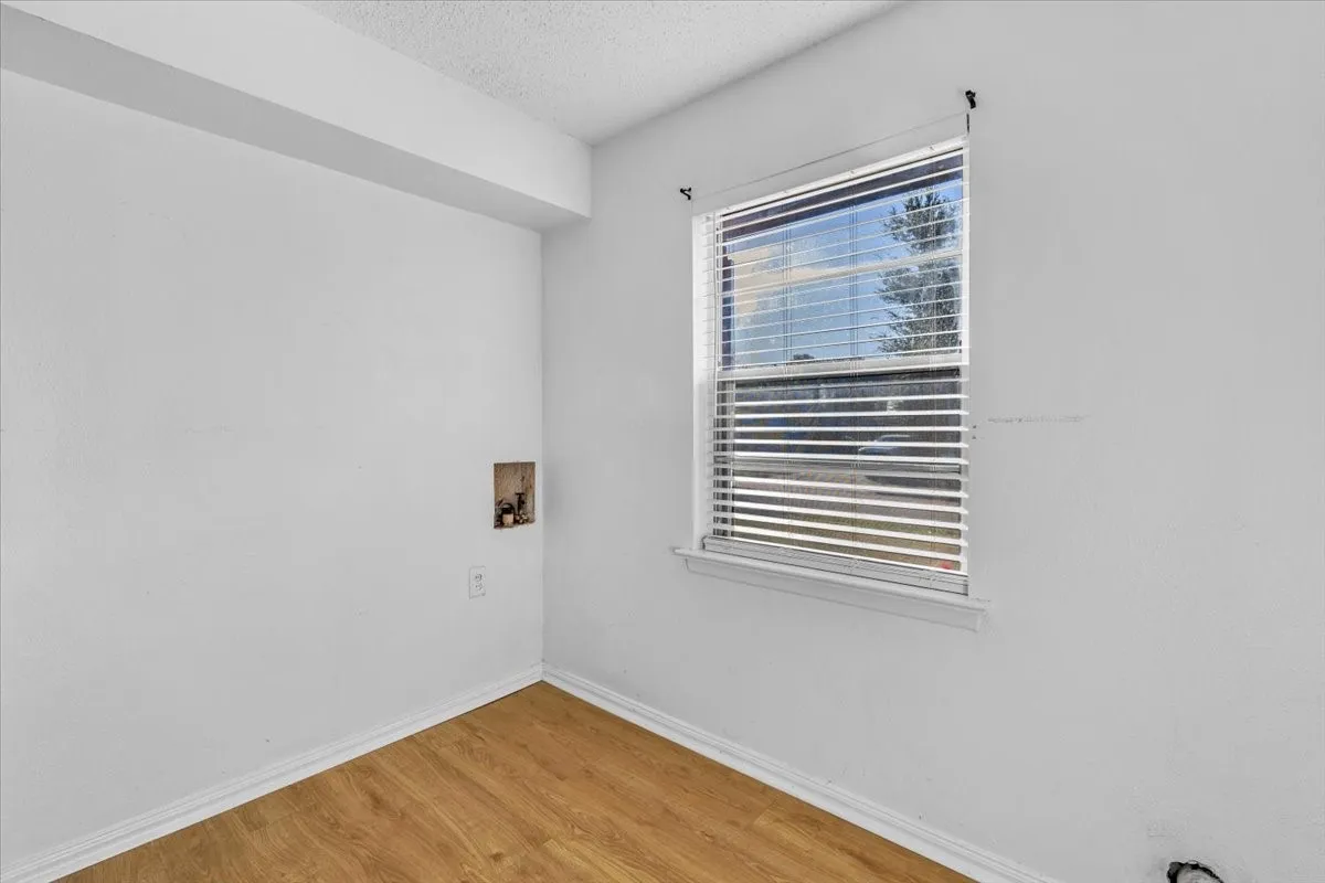 Wood-finish flooring with white baseboards, a window with horizontal blinds, and a utility hookup recess