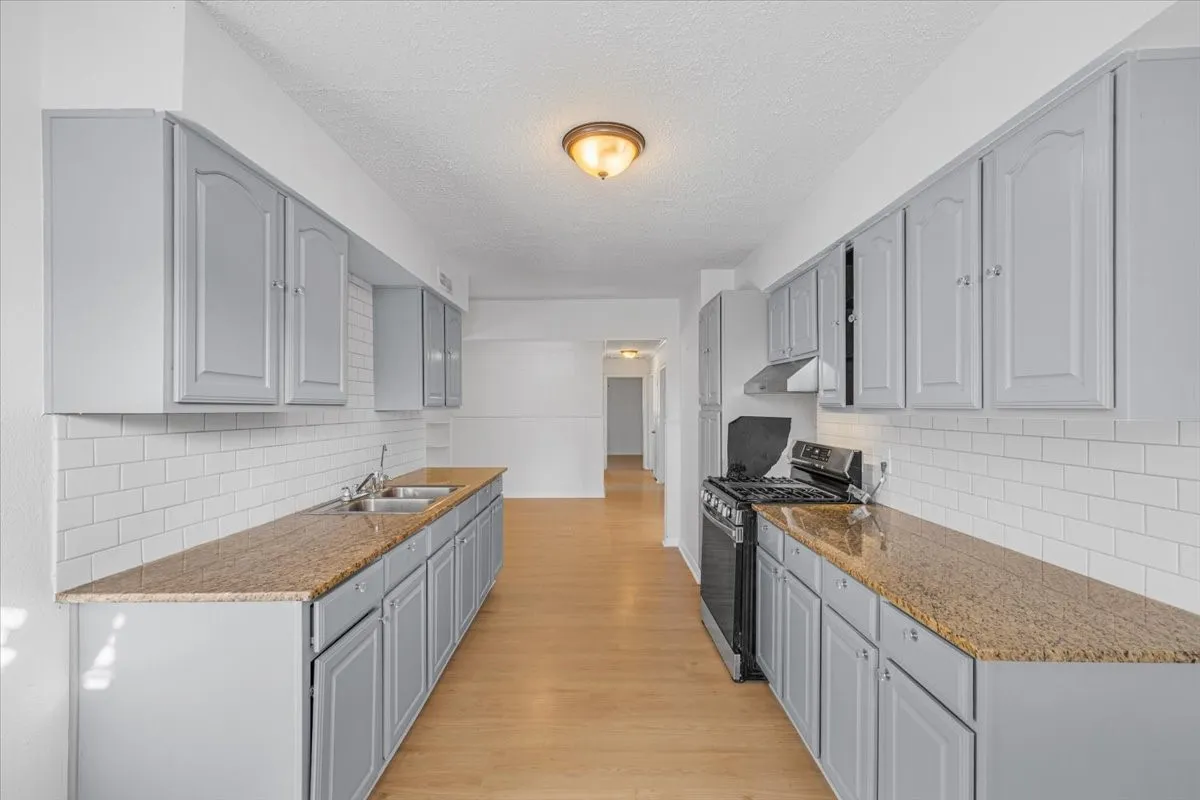 Kitchen featuring light gray cabinetry, granite-style countertops, white subway tile backsplash, and wood-finish flooring