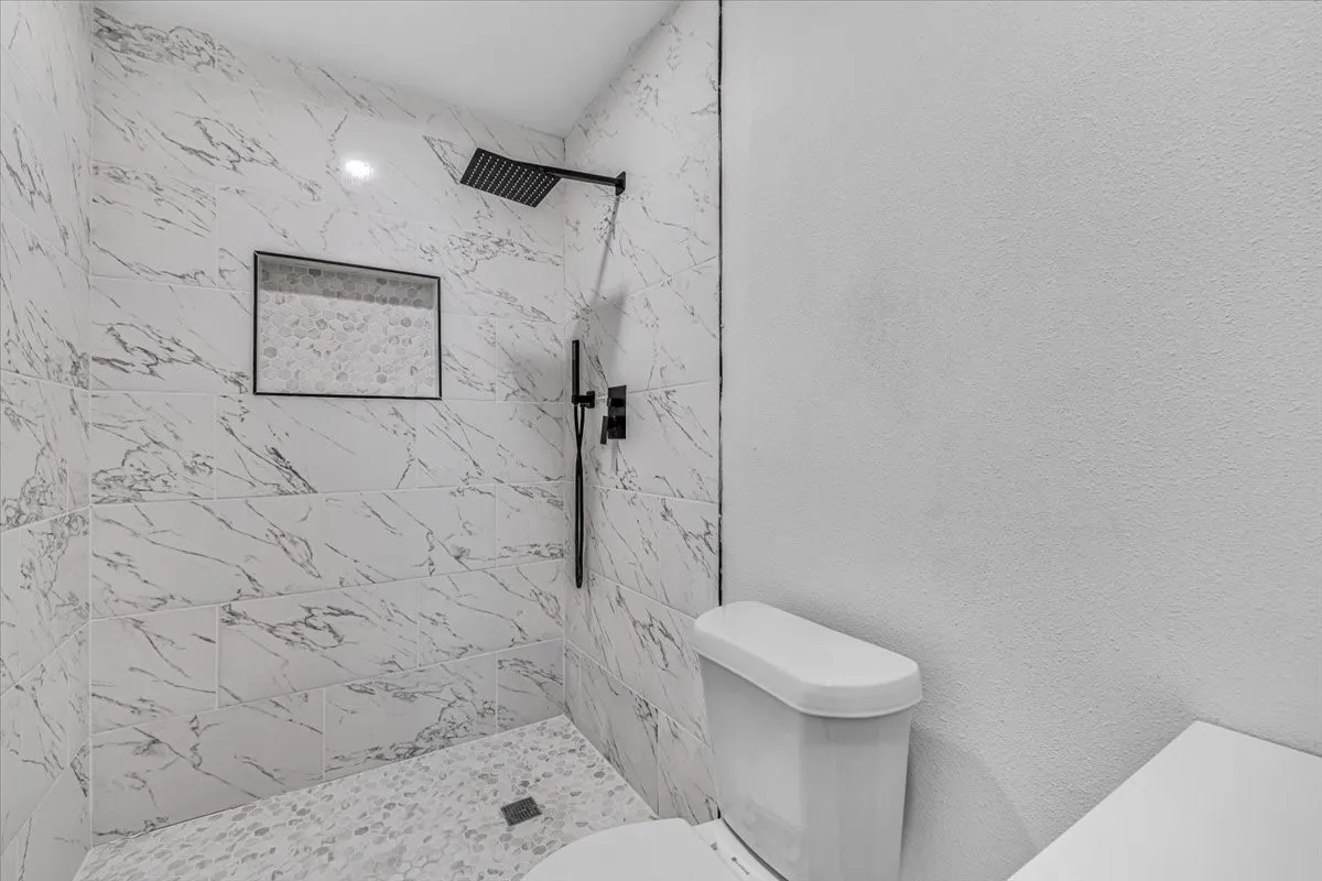 Tiled shower with matte black fixtures, an integrated shower niche, and a contrasting pebble-style shower floor