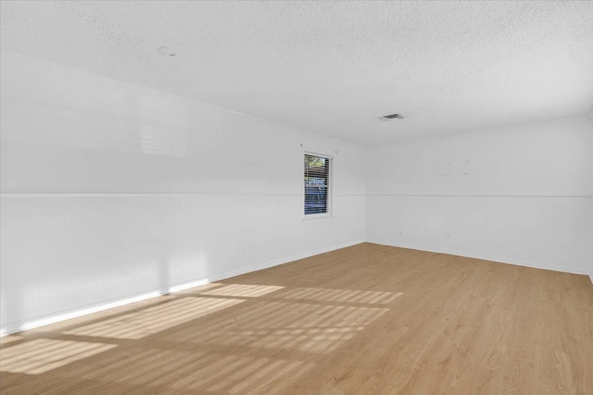 Wood-finish flooring, white walls, horizontal wall paneling, and a single window with blinds