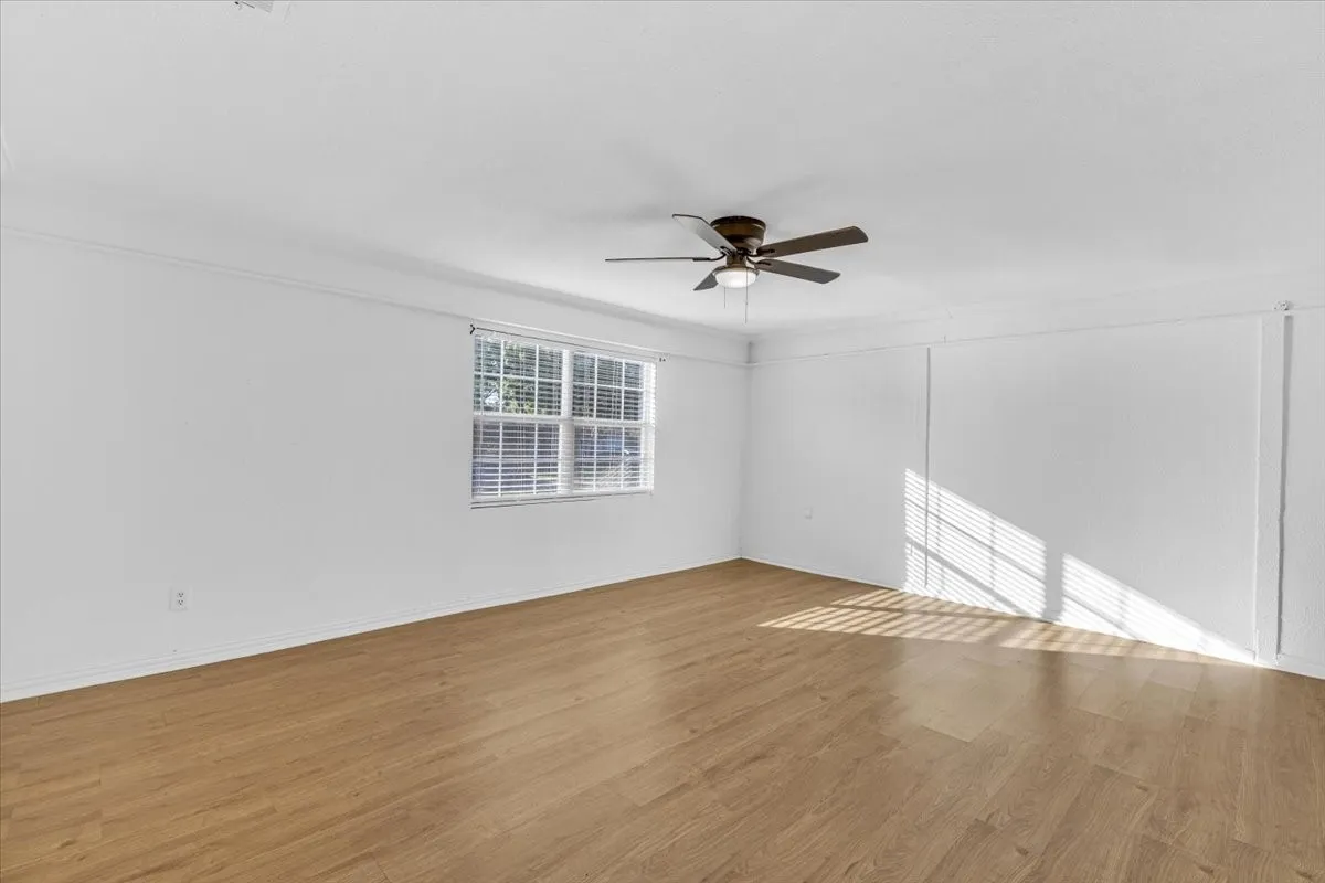 Wood-finish flooring, white painted walls, window with blinds, and a ceiling fan with integrated lighting