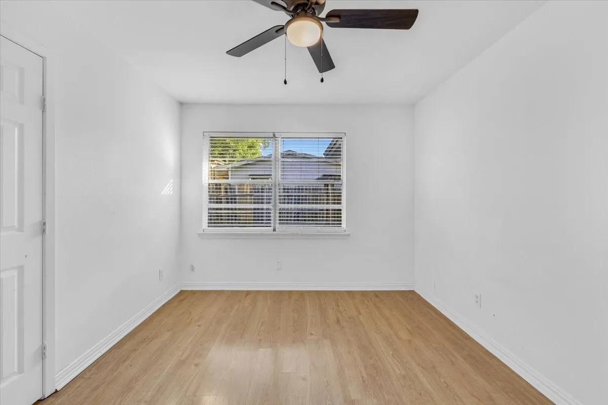 Wood-finish flooring, a window with horizontal blinds, and a ceiling fan with integrated lighting
