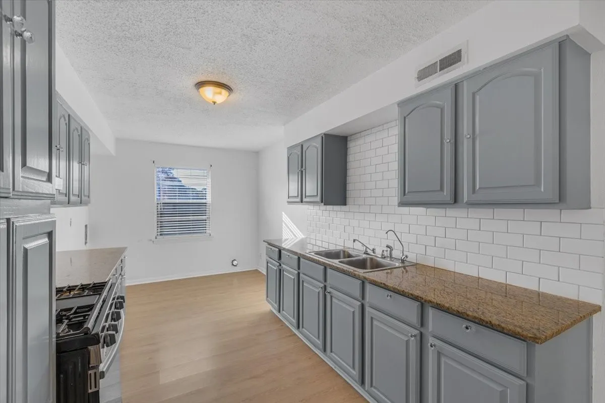 Kitchen featuring gray cabinetry, a subway tile backsplash, a double basin sink, and wood-finish flooring