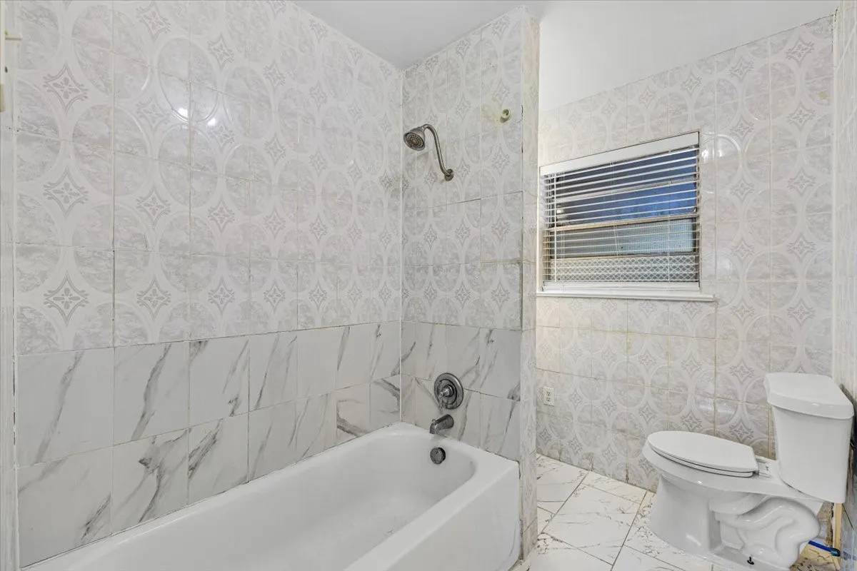 White ceramic bathtub with a shower fixture, white toilet, and patterned tile walls and flooring