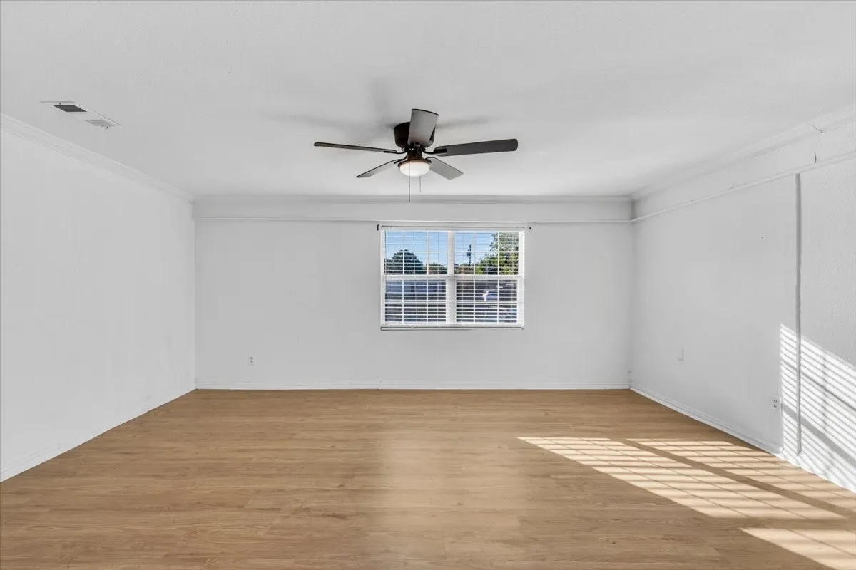 Spacious room featuring wood-finish flooring, a ceiling fan, and crown molding