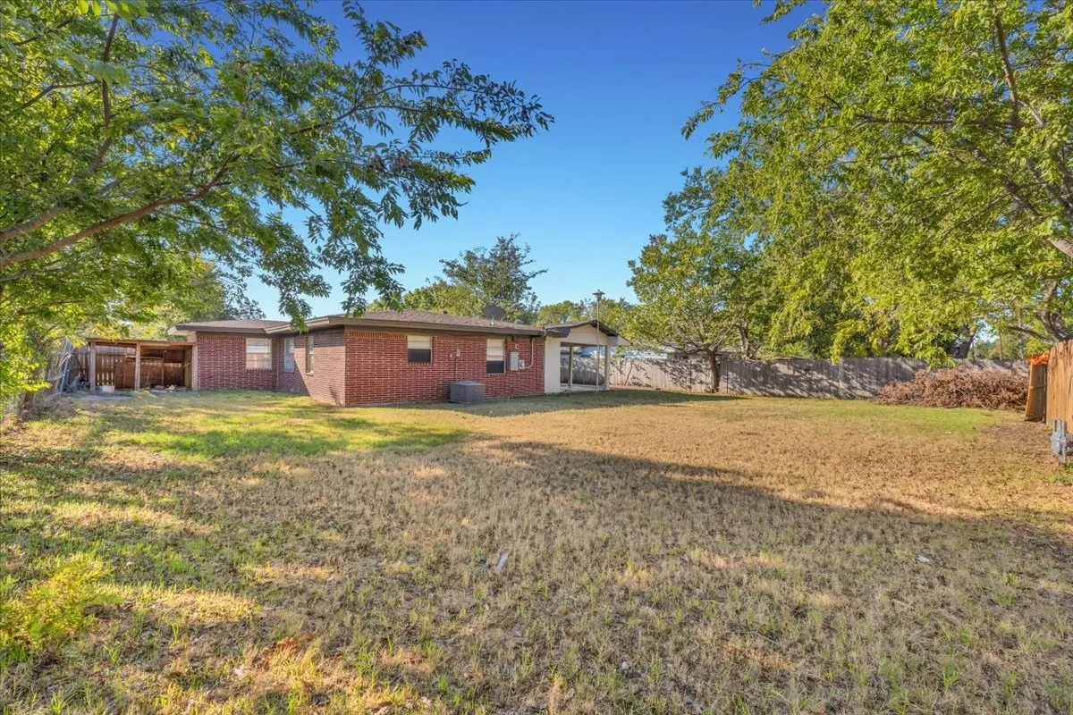 Expansive backyard with a brick exterior, covered patio, and mature trees