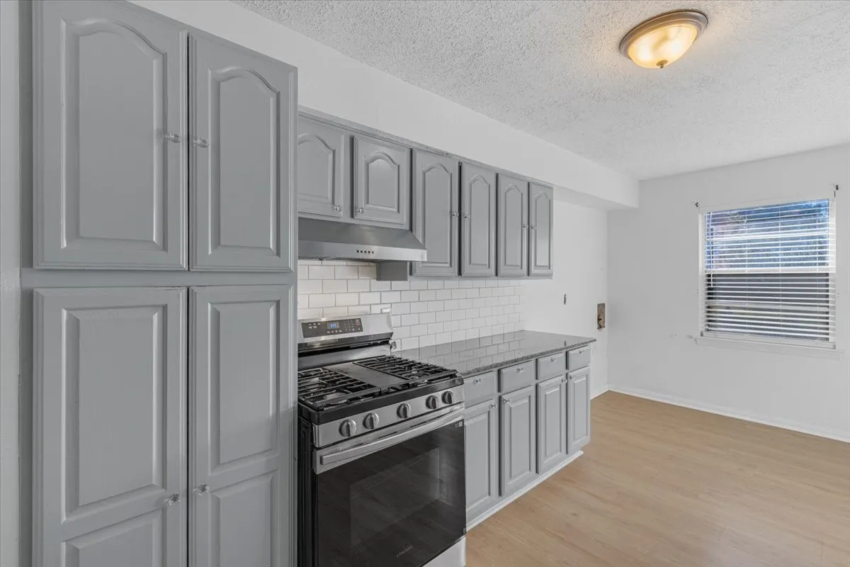 Gray cabinetry with silver hardware, stainless steel range and hood, white subway tile backsplash, light wood-finish flooring, and a flush mount ceiling light