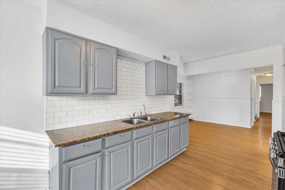Kitchen featuring gray cabinetry, dual basin sink, subway tile backsplash, and light wood-finish flooring