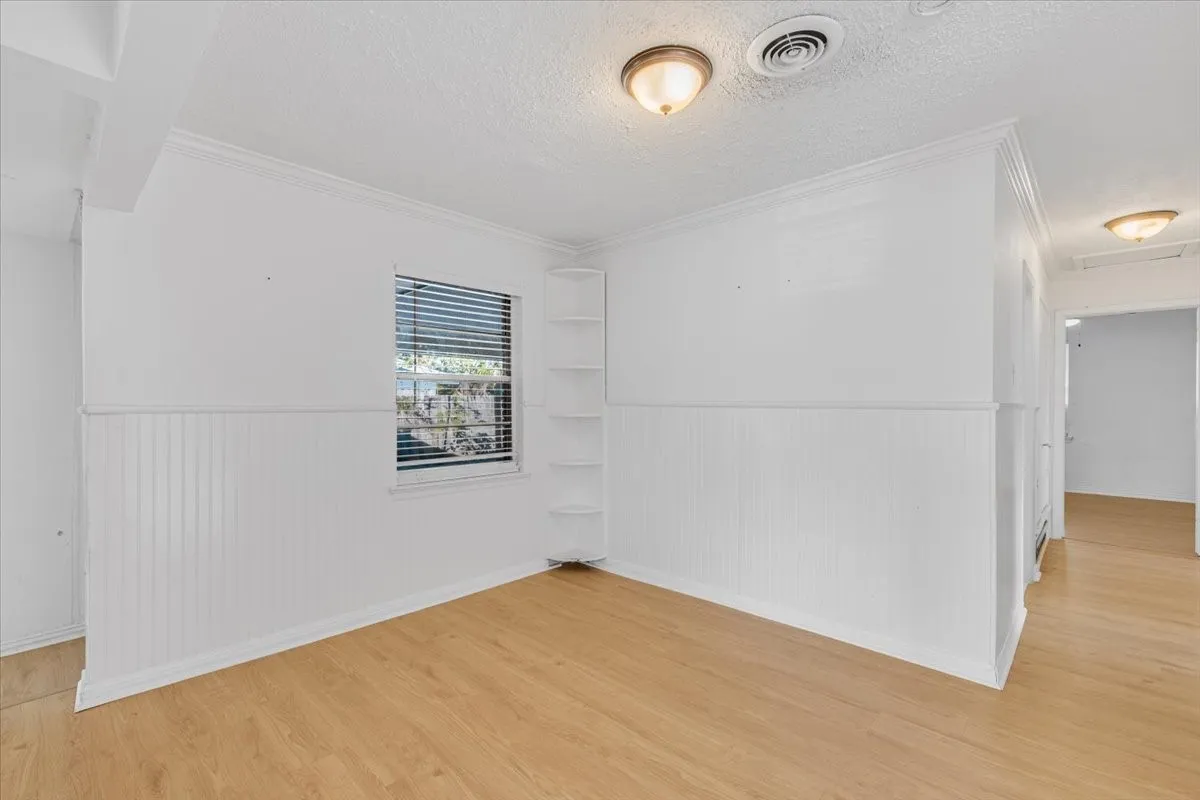 Light wood-finish flooring, white beadboard wainscoting, crown molding, built-in corner shelving, and ceiling-mounted lighting fixtures