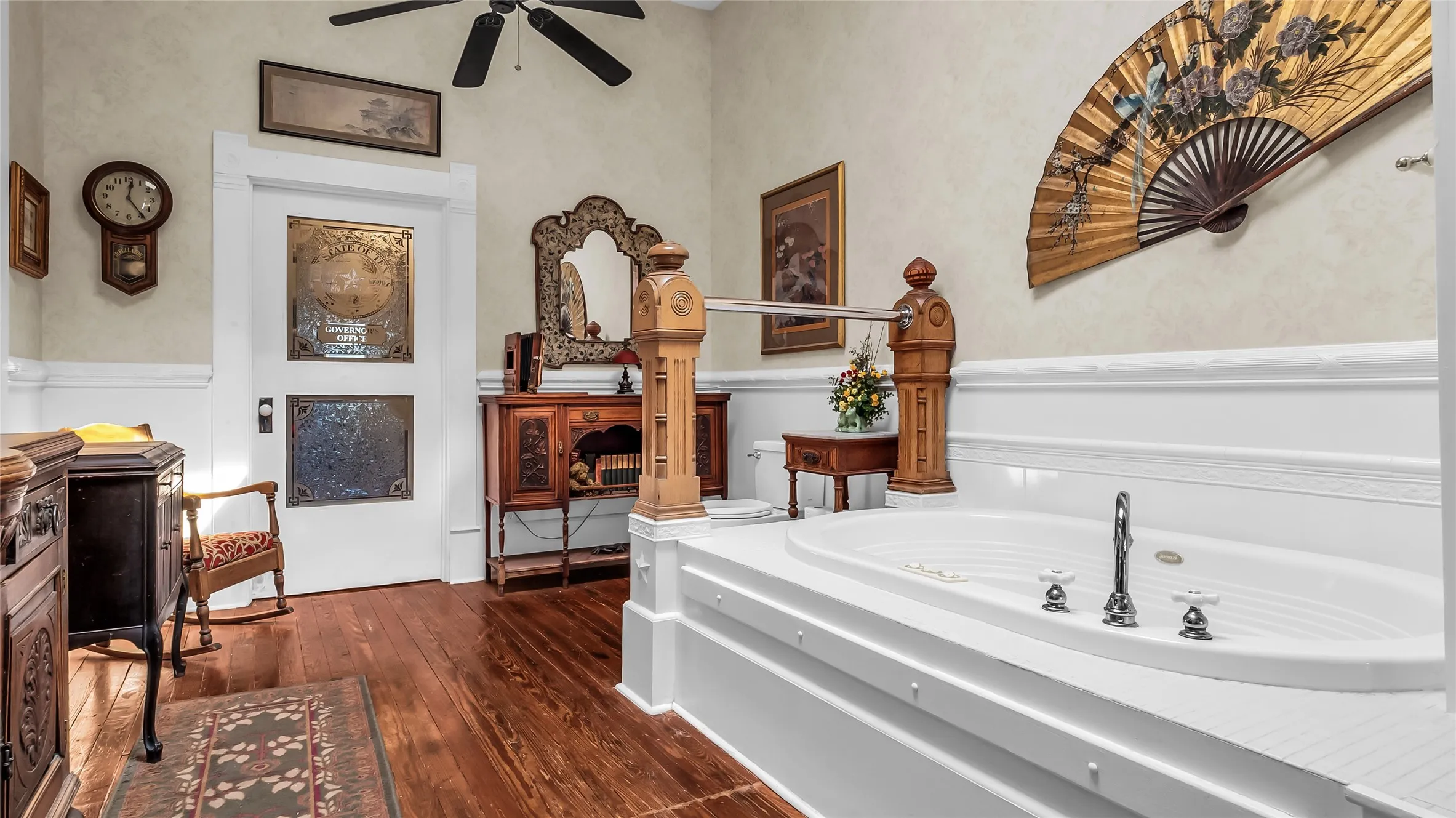 Platform jetted tub with chrome fixtures, wood-finish flooring, and a ceiling fan