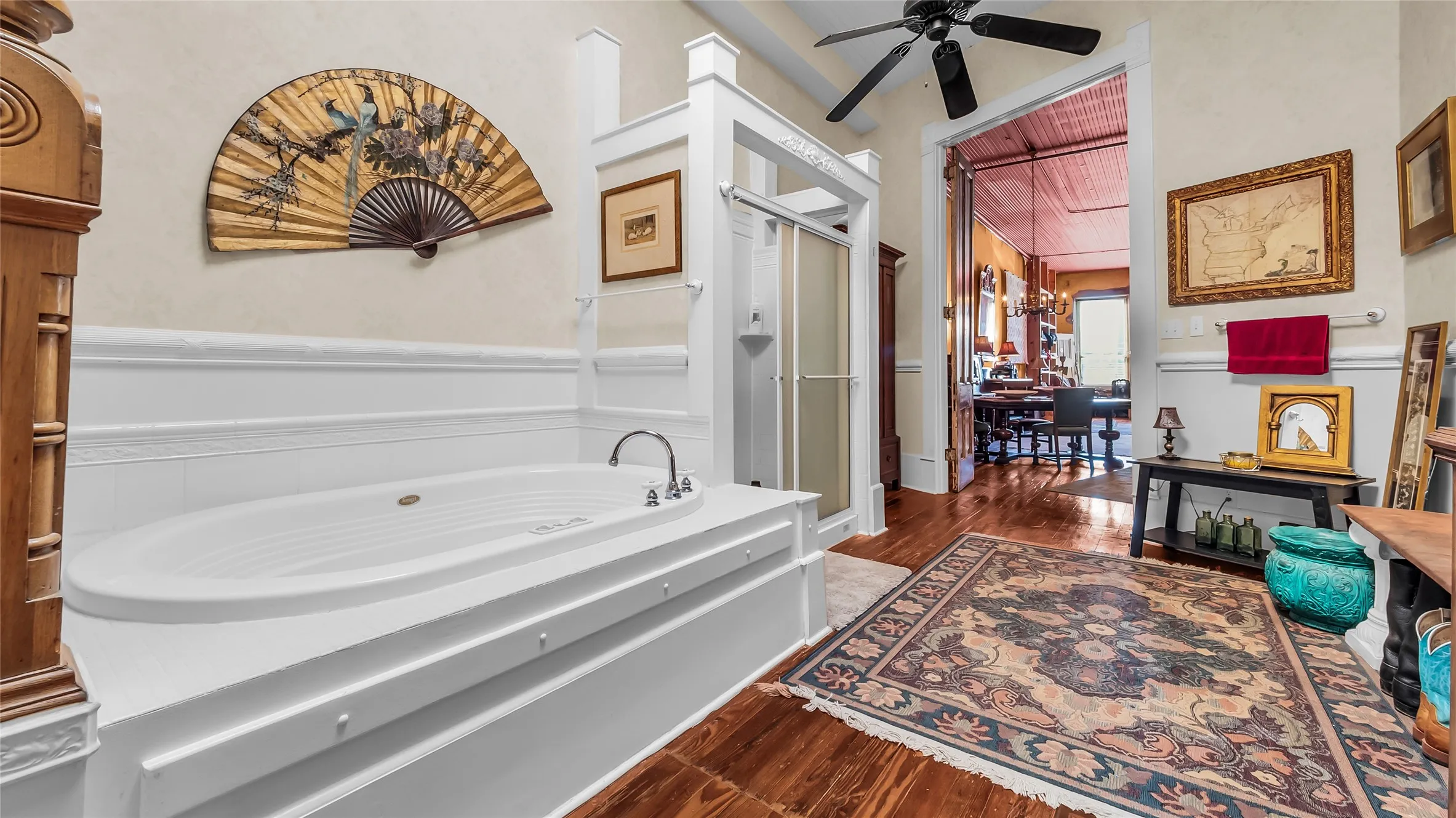 Spacious bathroom featuring a built-in soaking tub, separate shower enclosure with frosted glass, wood-finish flooring, and a ceiling fan