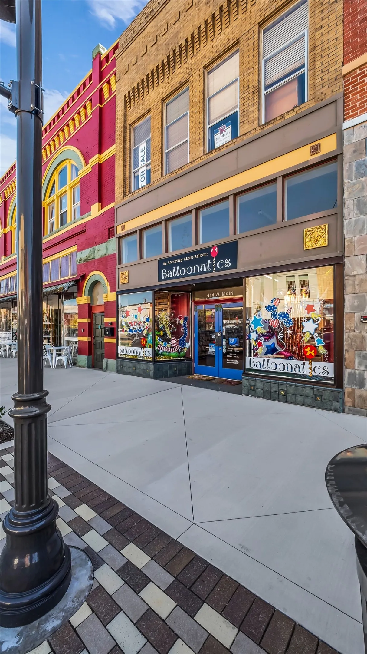 Brick facade building featuring a ground-level storefront, upper-level windows, and a patterned paver sidewalk