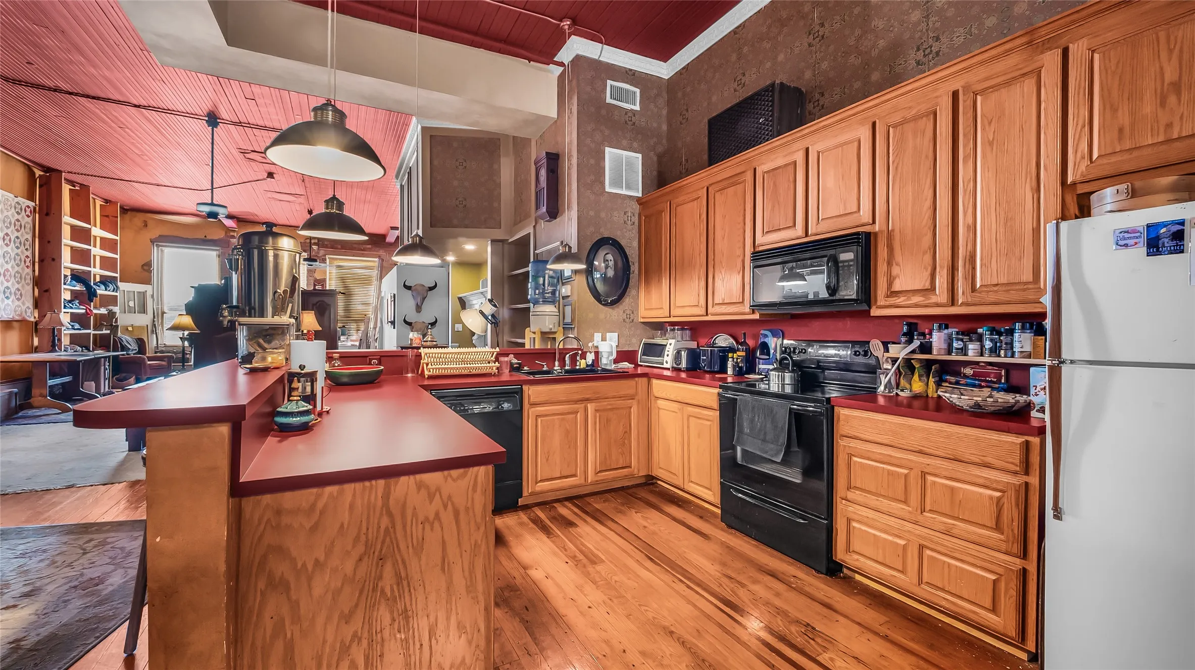 Wood-finish flooring, wood cabinetry, red countertops, black built-in oven, and a built-in microwave