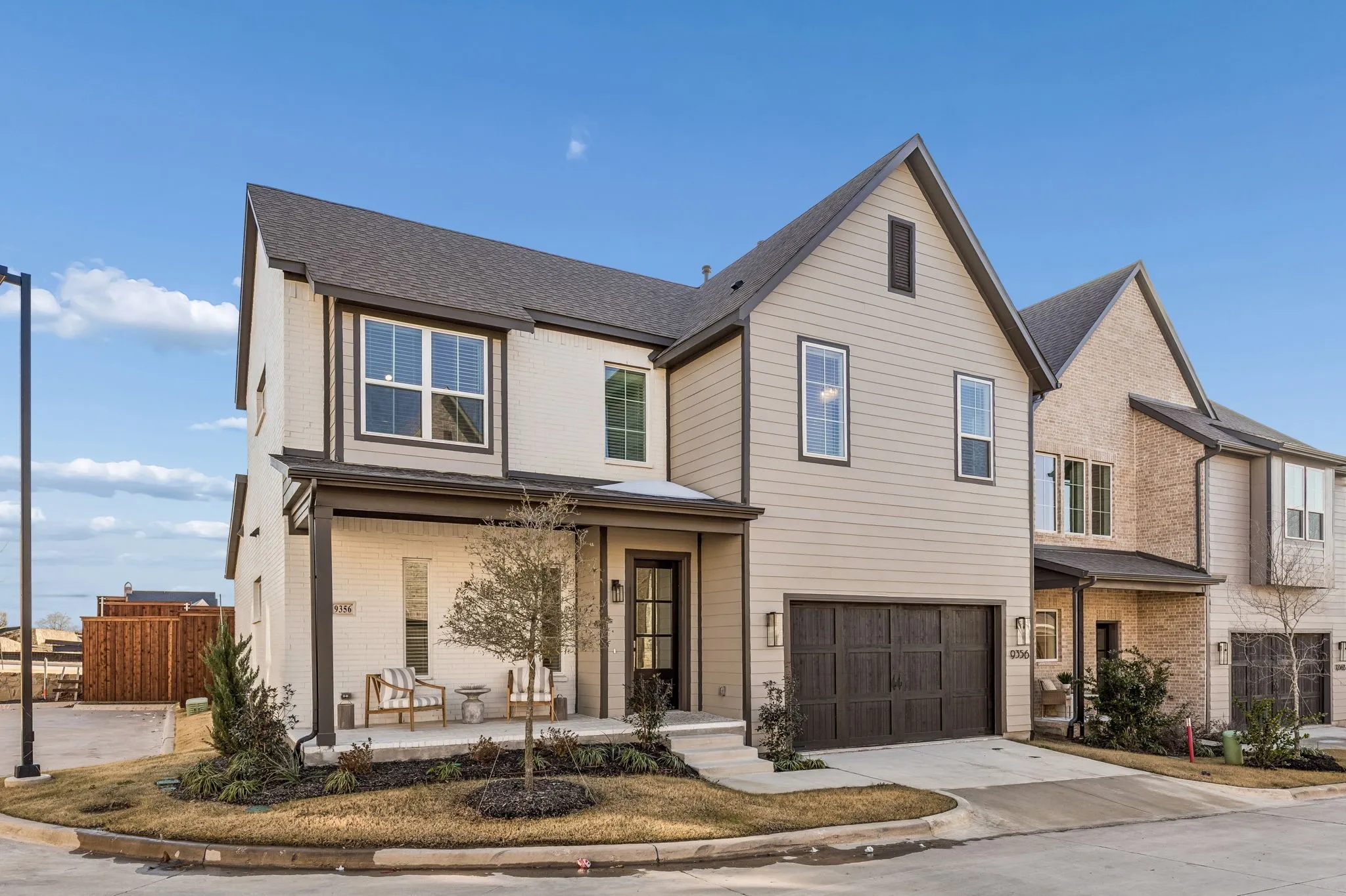 Contemporary architecture featuring a combination of light brick and horizontal siding, a dark asphalt shingle roof, a covered front porch, and an attached two-car garage