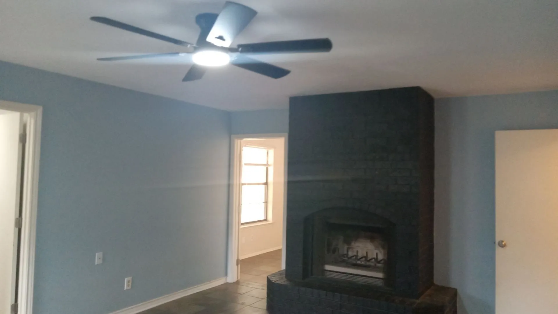 Spacious living area featuring light blue walls, wood-finish flooring, and a striking black fireplace surround with gas insert