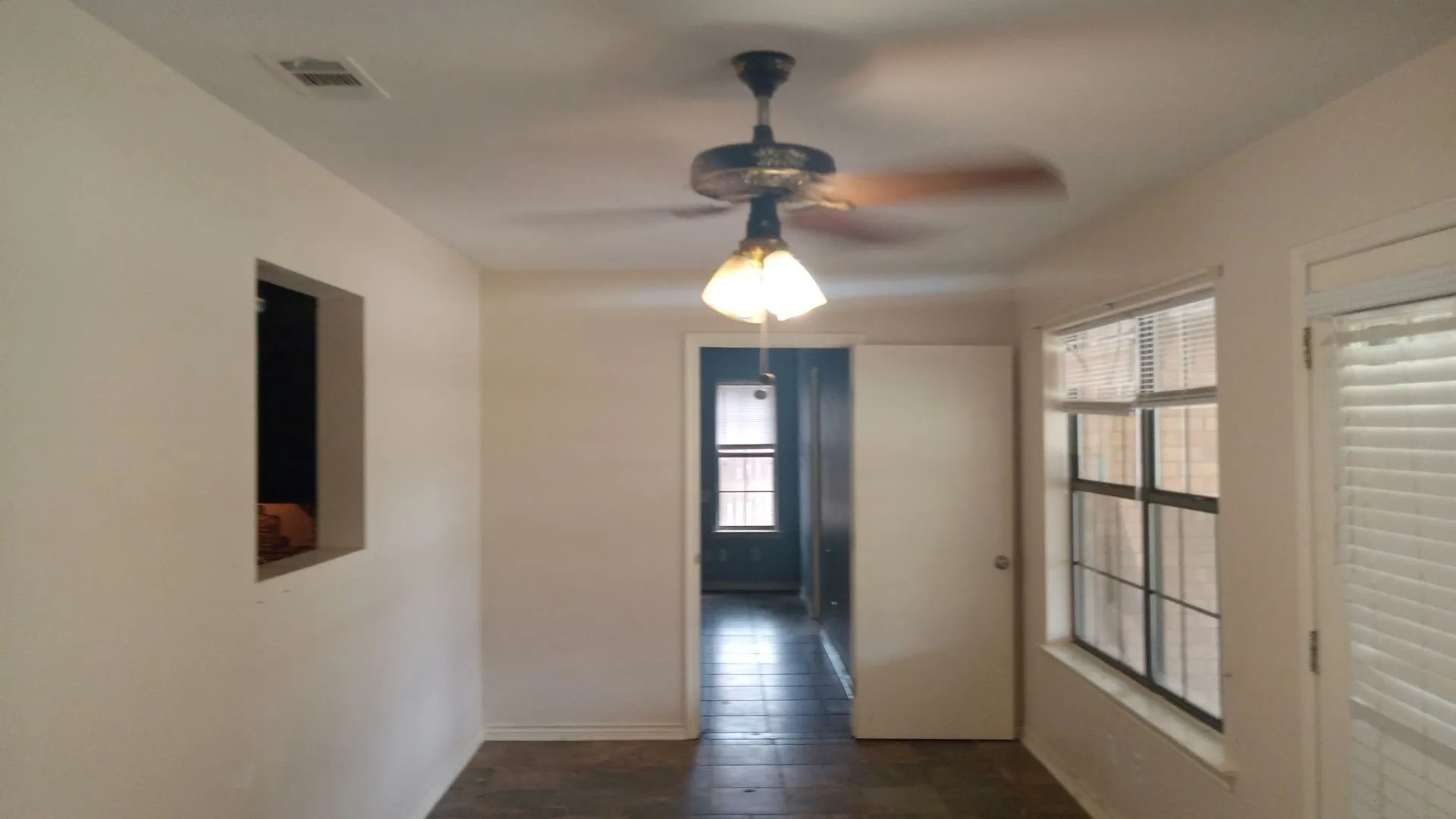 Ceiling fan with light fixture, window with blinds, interior door, and a wall cutout