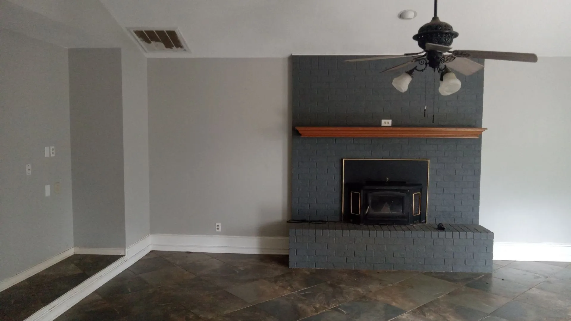 Floor-to-ceiling brick fireplace with a wood mantle, integrated wood-burning insert, and slate-style flooring