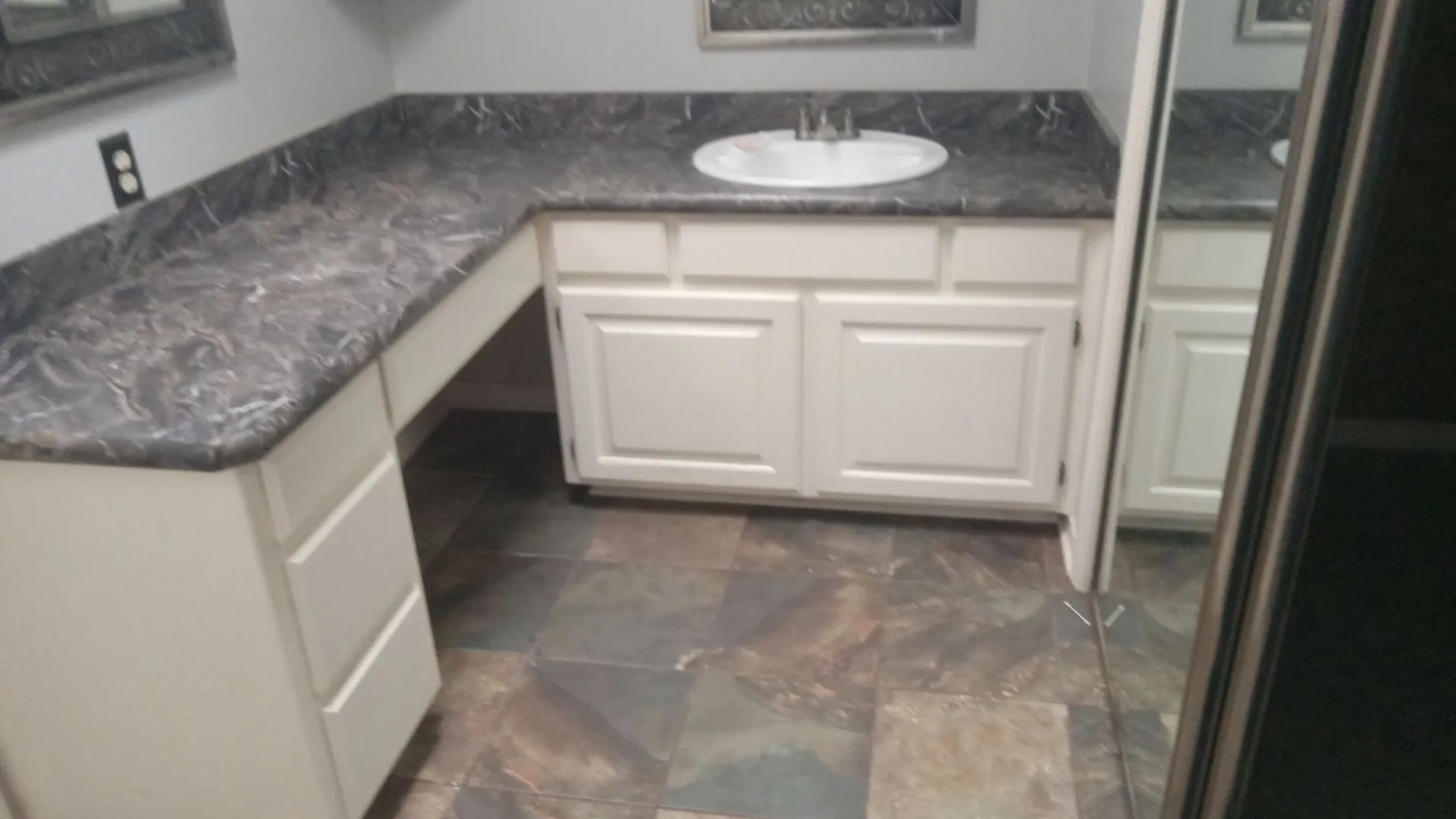L-shaped vanity with integrated sink, white cabinetry, dark patterned countertop, and multi-toned tile flooring