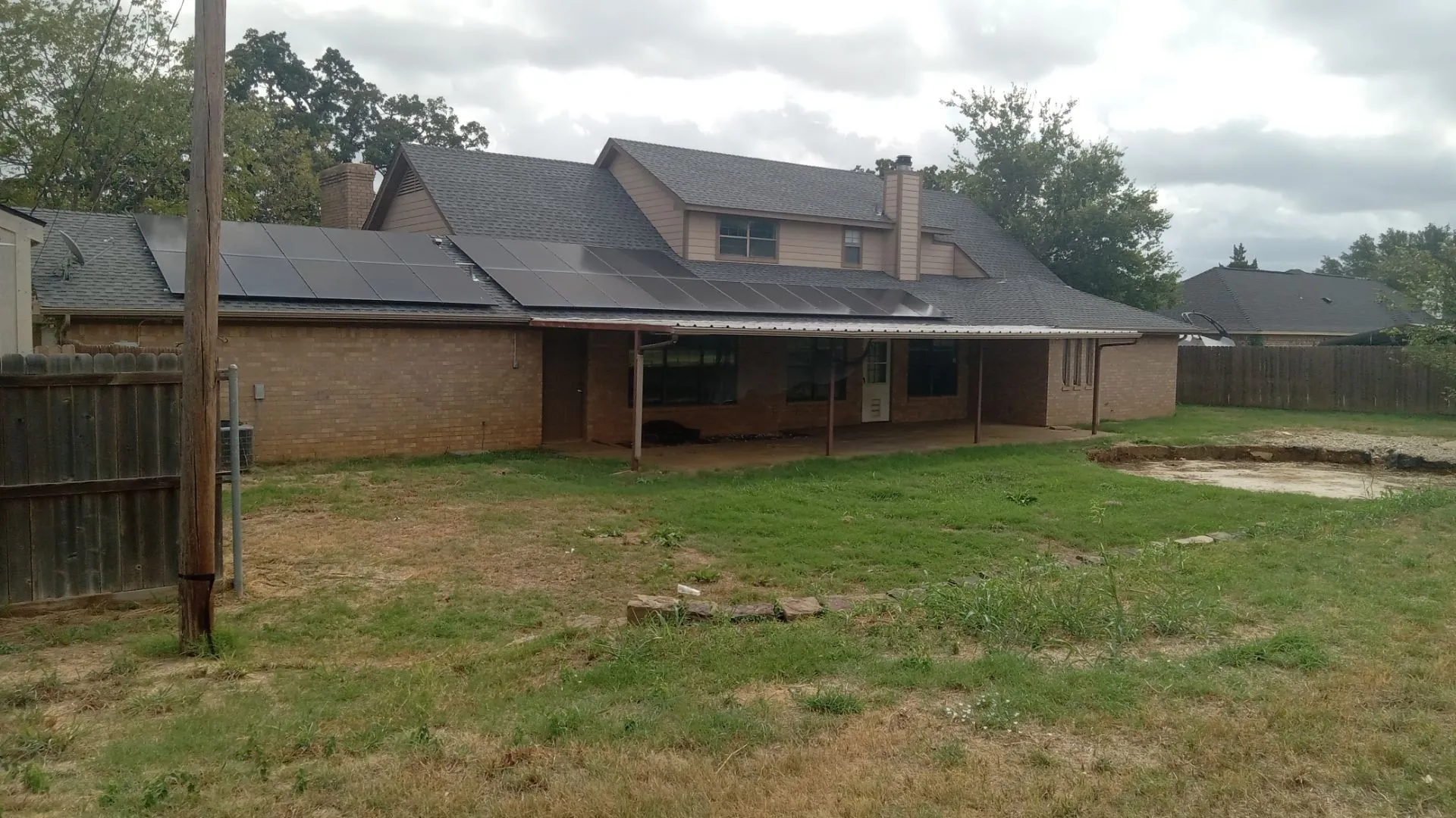 Brick exterior with a covered patio, solar panels, and a wood privacy fence