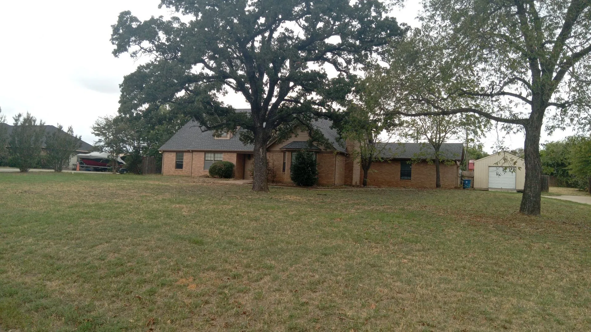 Brick exterior home with a gabled roof, mature trees, and an accessory building with a garage door