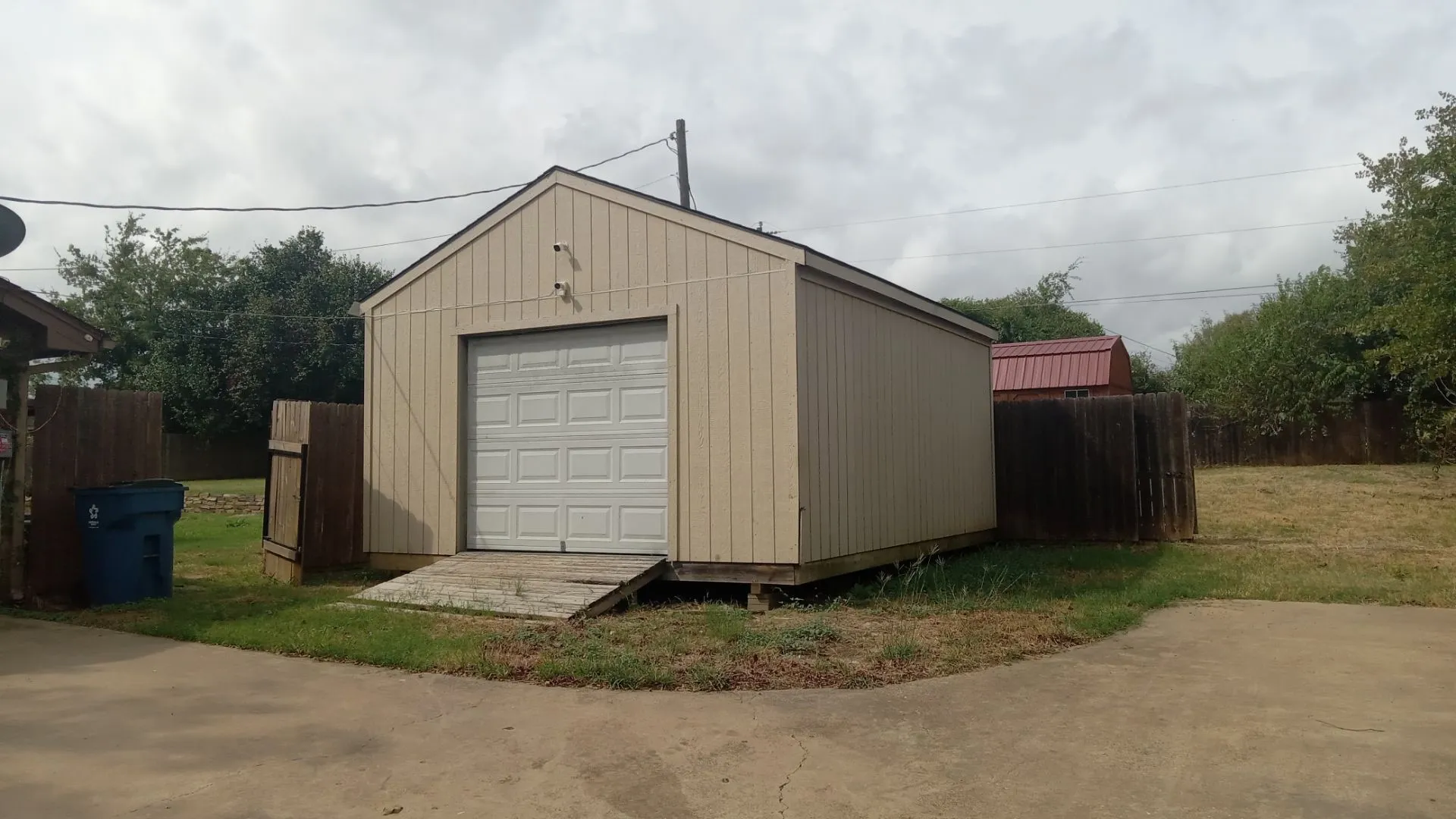 Detached storage shed with roll-up garage door and an adjacent wooden fence