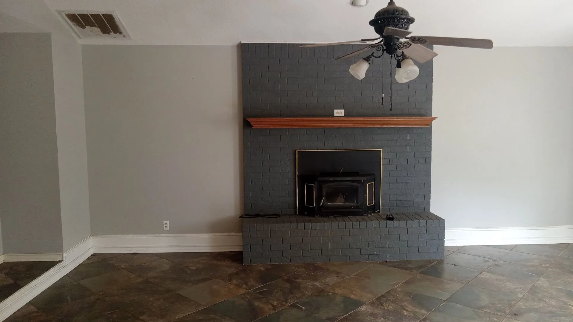 Brick fireplace with wood mantel, tile flooring, and ceiling fan