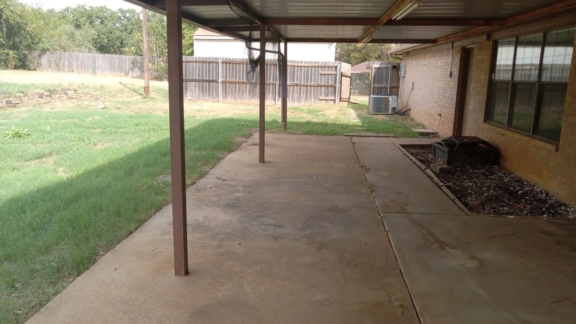 Covered patio with concrete flooring, supported by metal posts