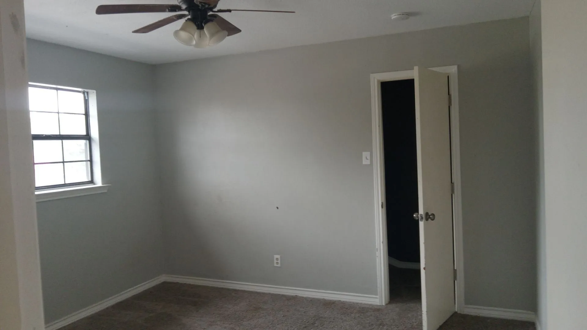 Carpeted room featuring a ceiling fan with integrated lighting, a window with grid inserts, and a door opening into an interior space