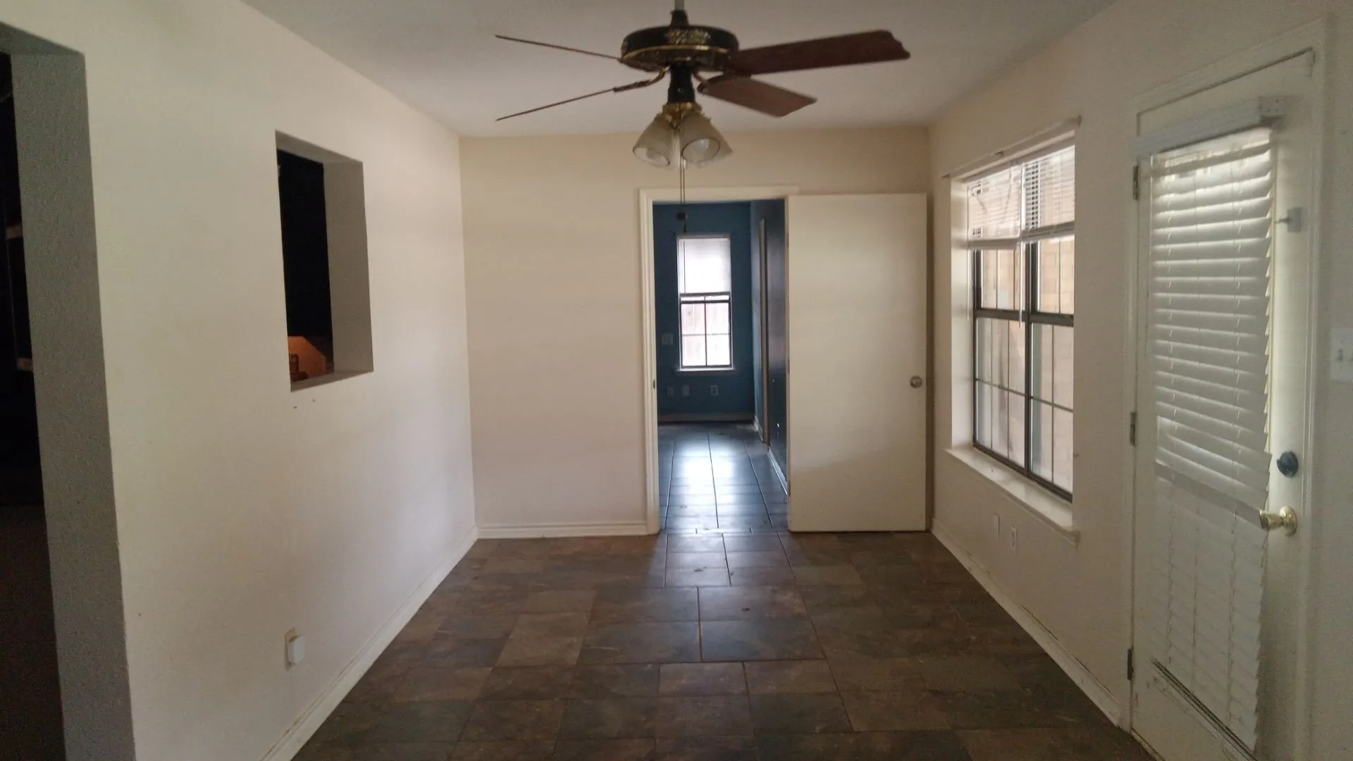 Tile flooring, ceiling fan with light fixture, interior window opening, window with blinds, and white door
