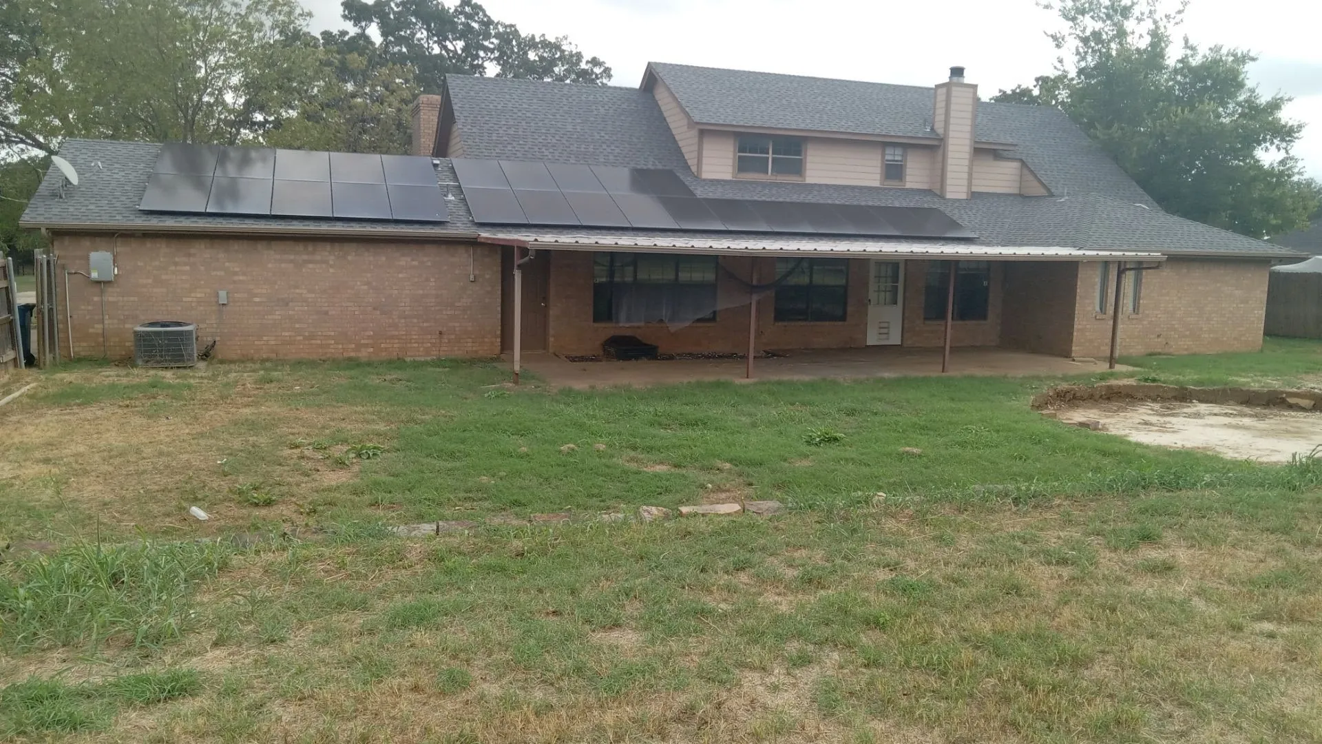 Brick exterior with a covered patio, solar panels, and a shingled roof