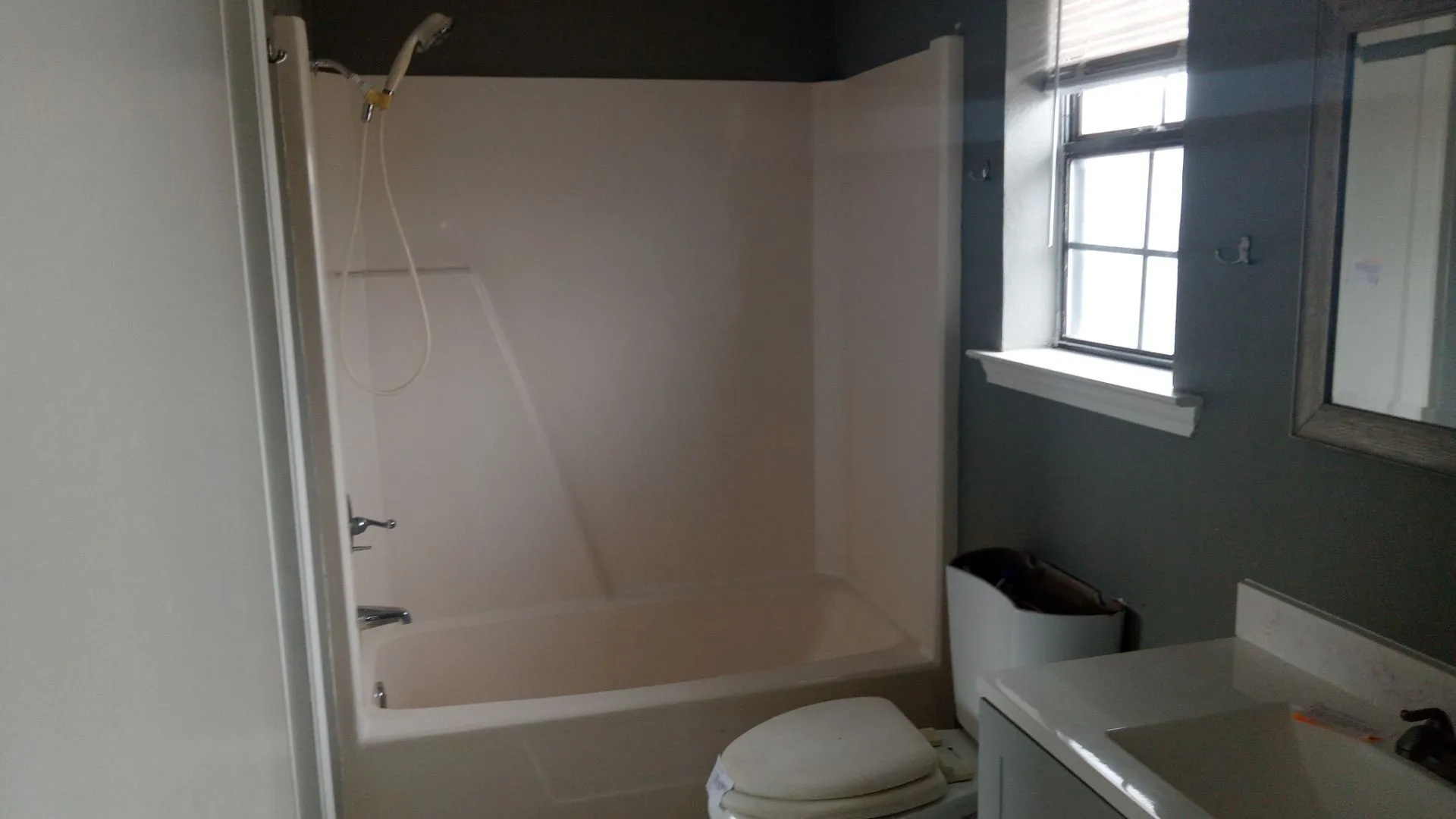 Bathroom featuring an integrated tub and shower unit, a single vanity with a white countertop and basin, and a window with blinds
